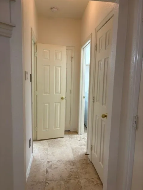 Hallway featuring neutral-toned tile flooring, recessed ceiling lighting, and multiple paneled doors with brass hardware