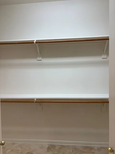 Storage closet featuring two levels of shelving and hanging rods