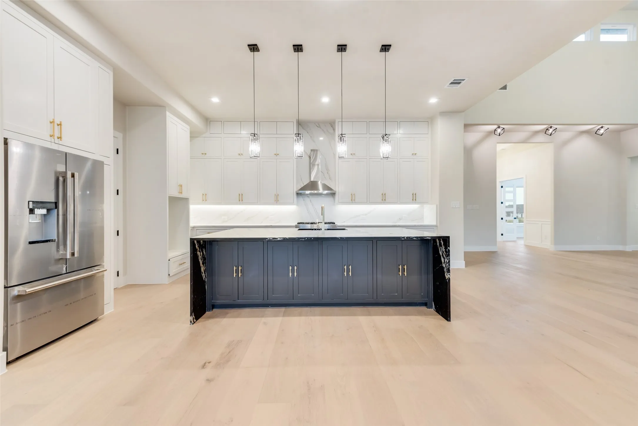 Kitchen featuring a dark-toned island with a waterfall countertop, light wood-finish flooring, and white cabinetry with gold-toned hardware