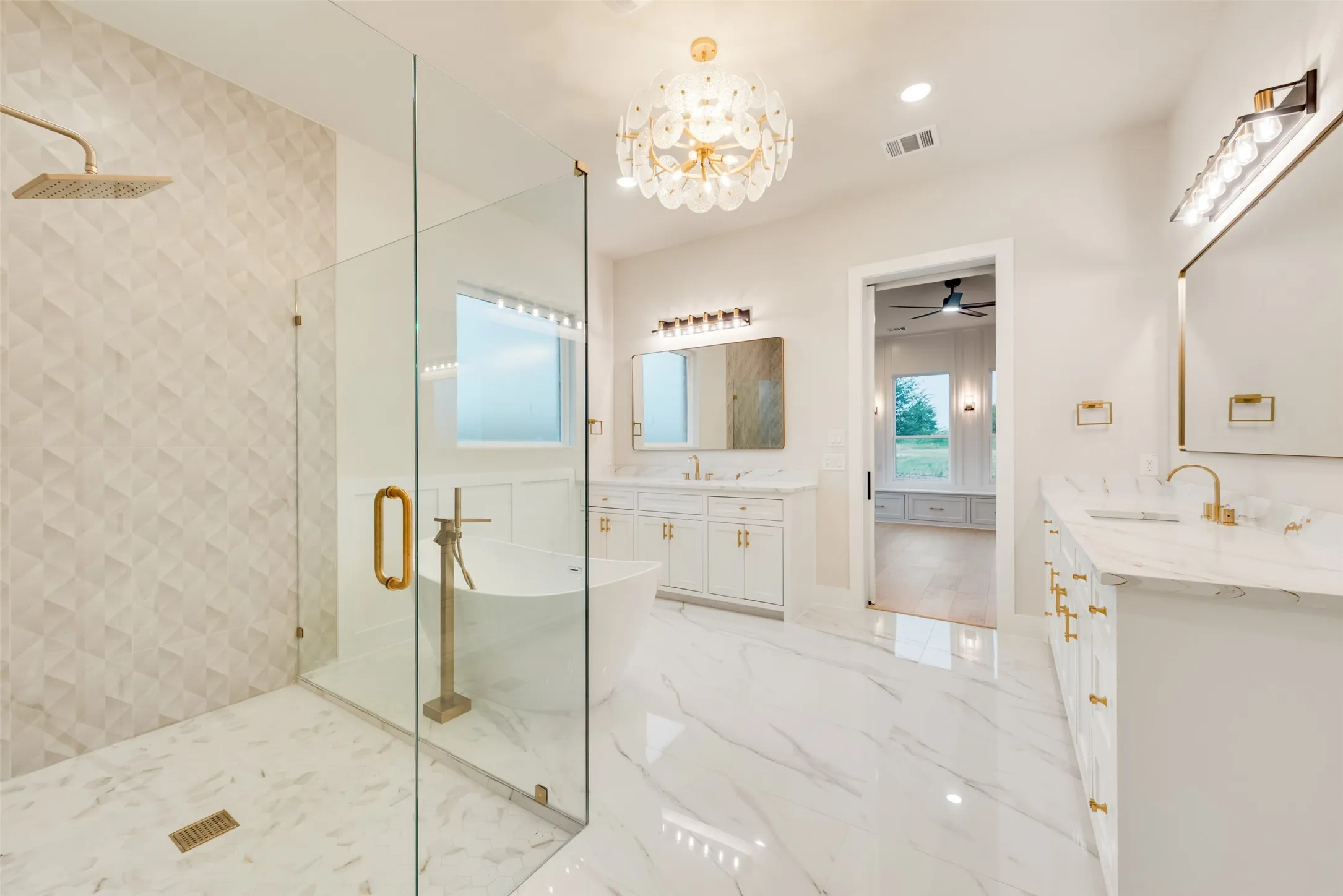 Spacious bathroom featuring a frameless glass shower enclosure, a freestanding soaking tub, and dual vanity areas with white cabinetry and marble-finish countertops