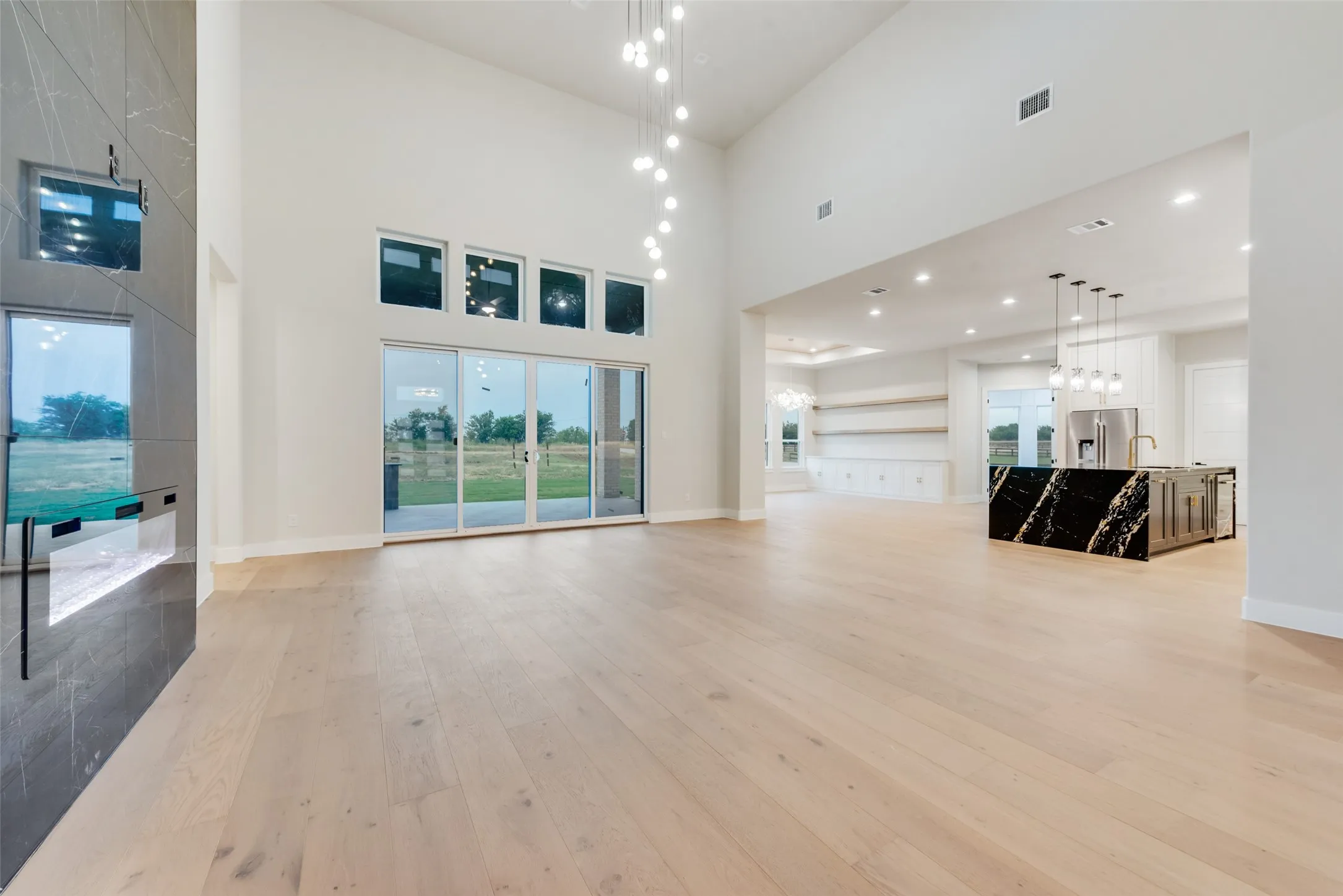 Spacious living area featuring high vaulted ceilings, light wood-finish flooring, and a contemporary linear electric fireplace