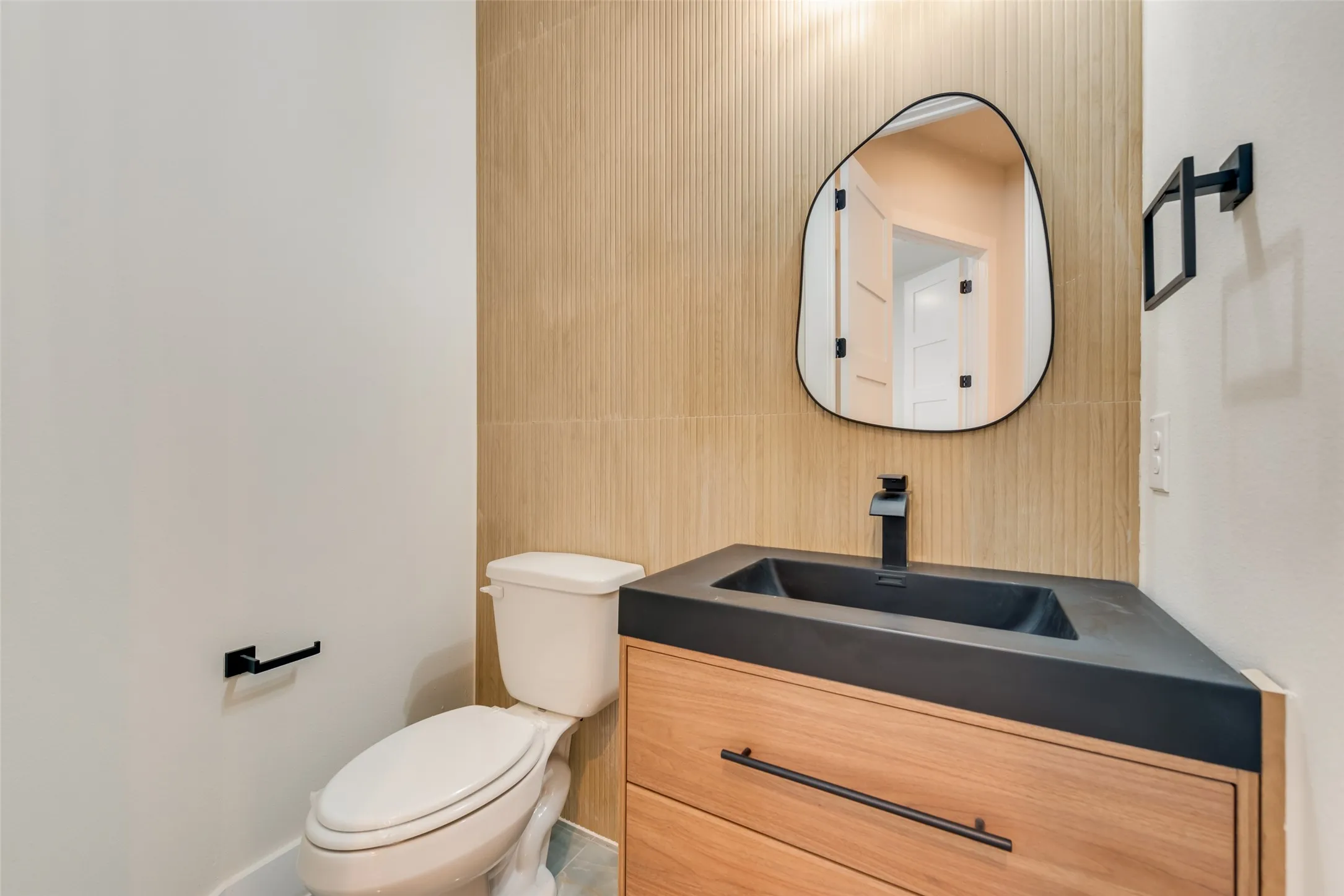 Powder room featuring a wood-finish vanity with a black integrated sink, matte black faucet, and a contemporary irregular-shaped mirror