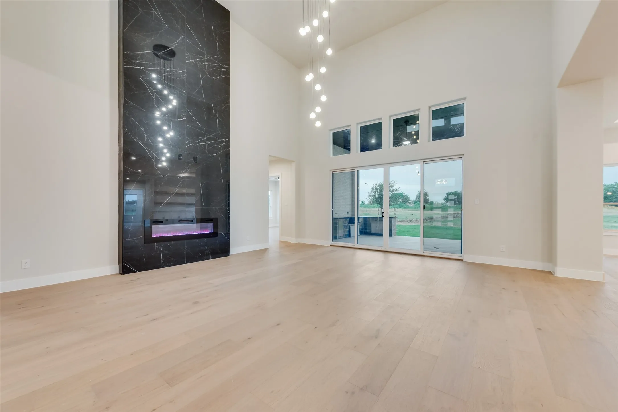 Vaulted living space featuring a floor-to-ceiling dark marble fireplace surround with an integrated linear fireplace, light wood-finish flooring, and a multi-pane glass sliding door opening to an outdoor area