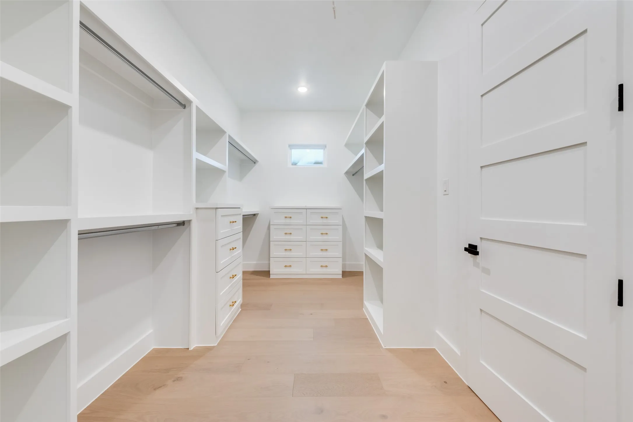 Expansive closet system featuring light wood-finish flooring, built-in shelving, hanging rods, and integrated drawer storage with brass hardware