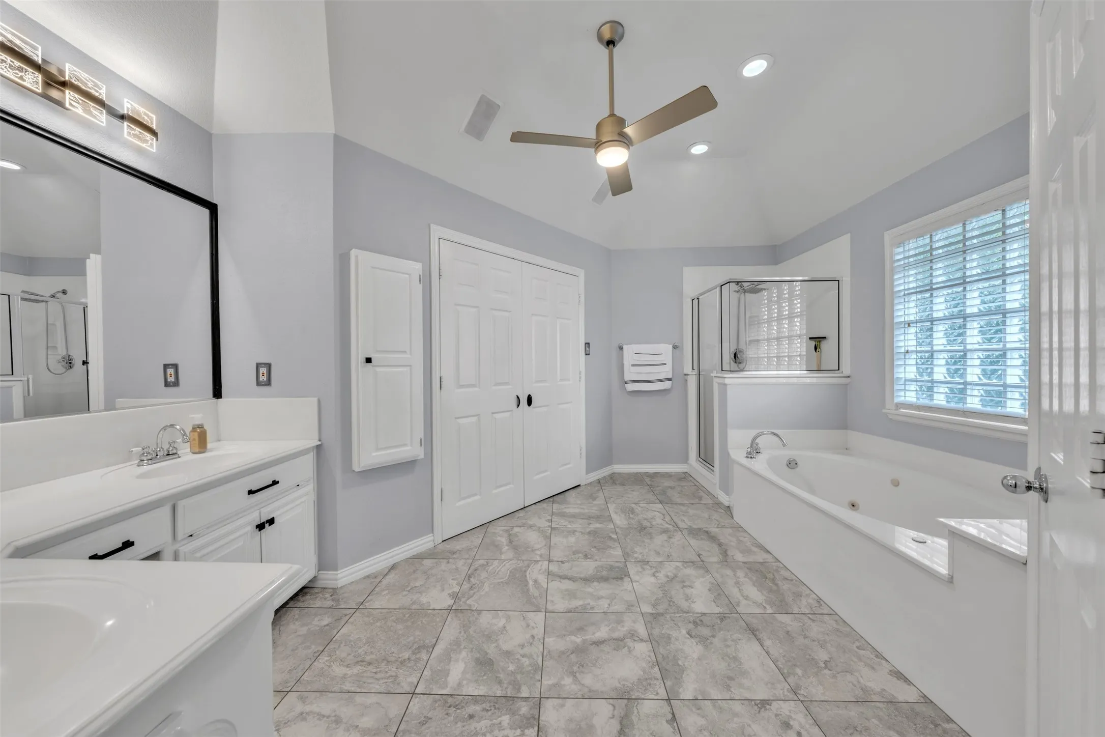 Spacious bathroom featuring a dual vanity, white cabinetry, a glass-enclosed shower, a built-in jetted tub, and tile flooring