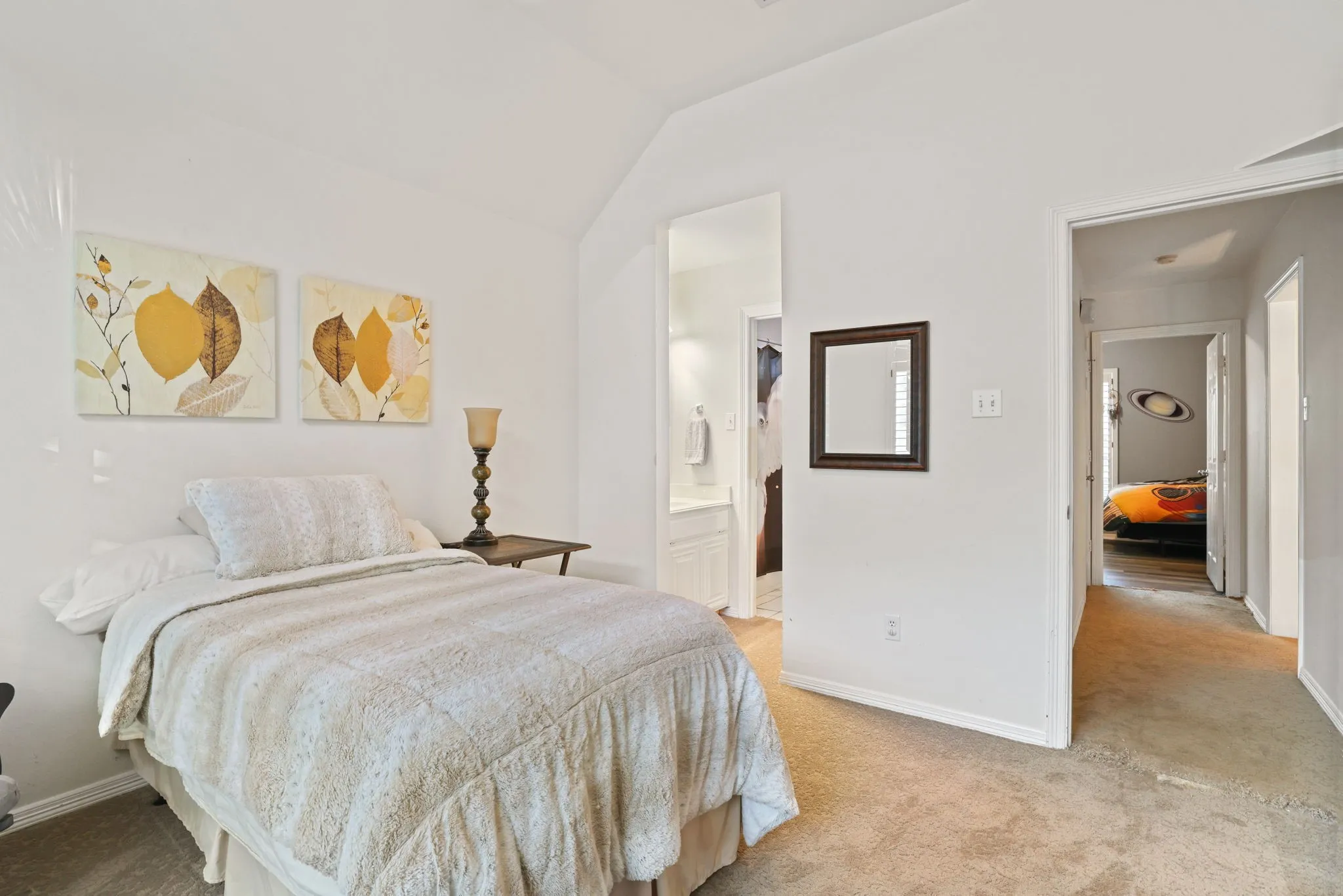 Bedroom with vaulted ceiling, plush carpeting, and direct access to a private bathroom featuring a vanity with built-in cabinetry