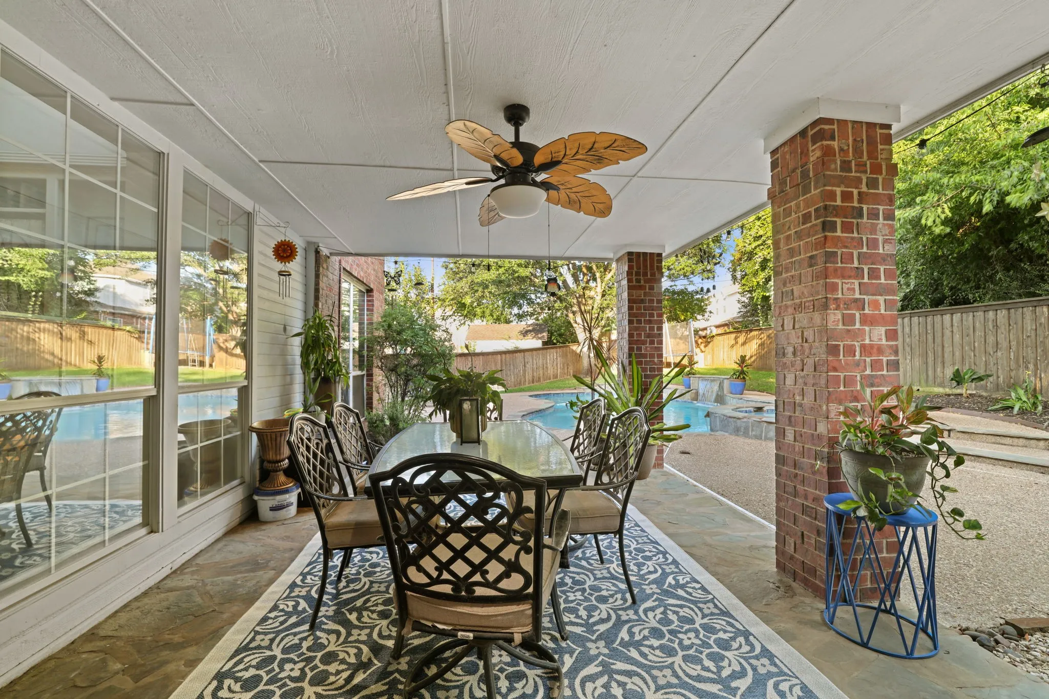 Covered patio featuring a ceiling fan, brick columns, and direct access to the backyard with a swimming pool