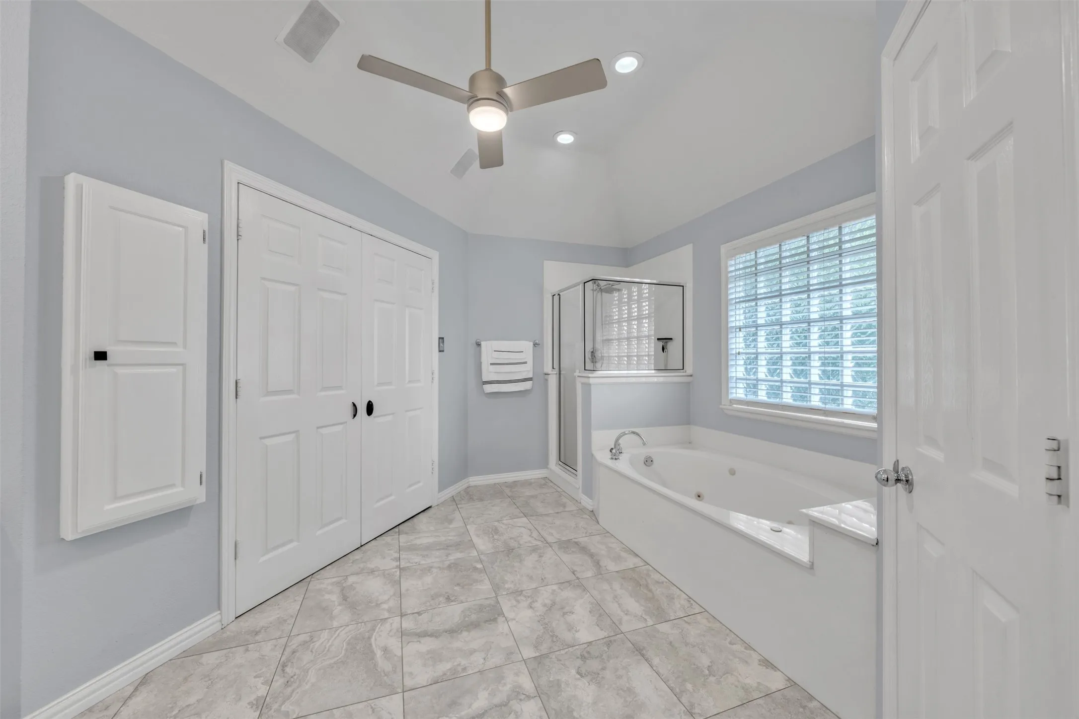 Vaulted ceiling with a ceiling fan, jetted soaking tub, glass block window, glass-enclosed shower, and tiled flooring