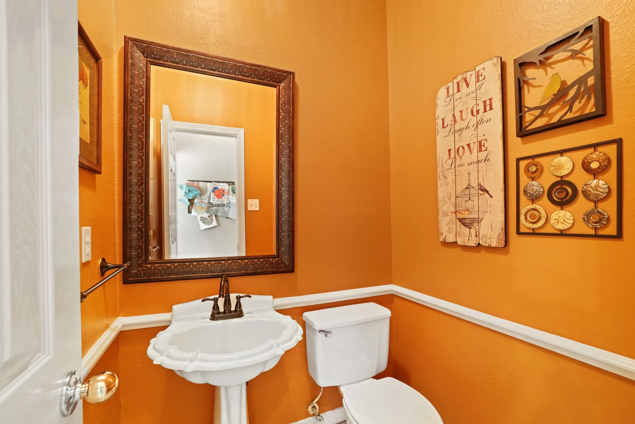 Pedestal sink with bronze-finish faucet, traditional wall mirror with ornate frame, white baseboard and chair rail molding, and a white toilet