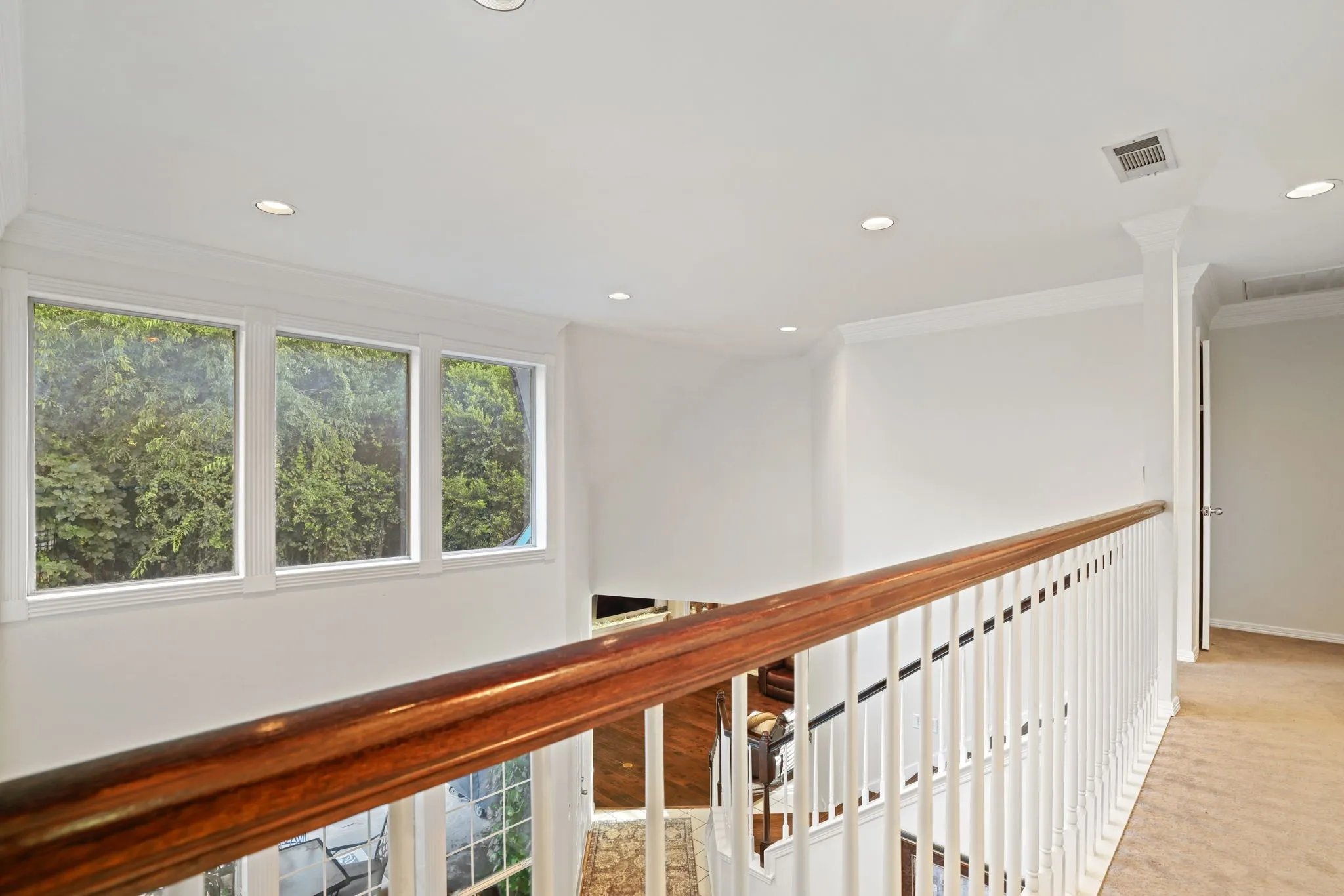 Second-story landing featuring a wood handrail, white balusters, and crown molding