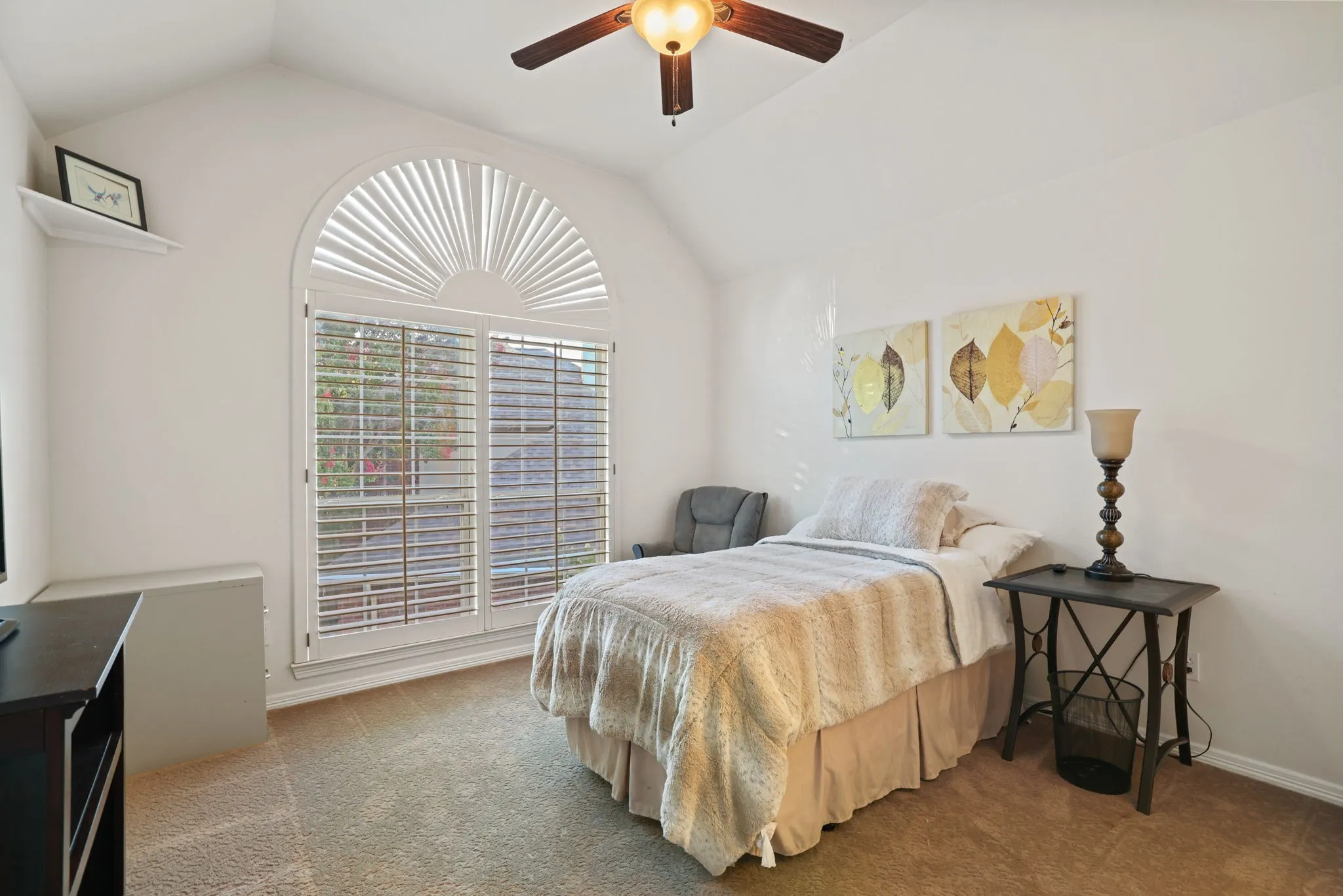 Vaulted ceiling room featuring a large arched window with plantation shutters, light-toned carpet flooring, and a ceiling fan with integrated lighting