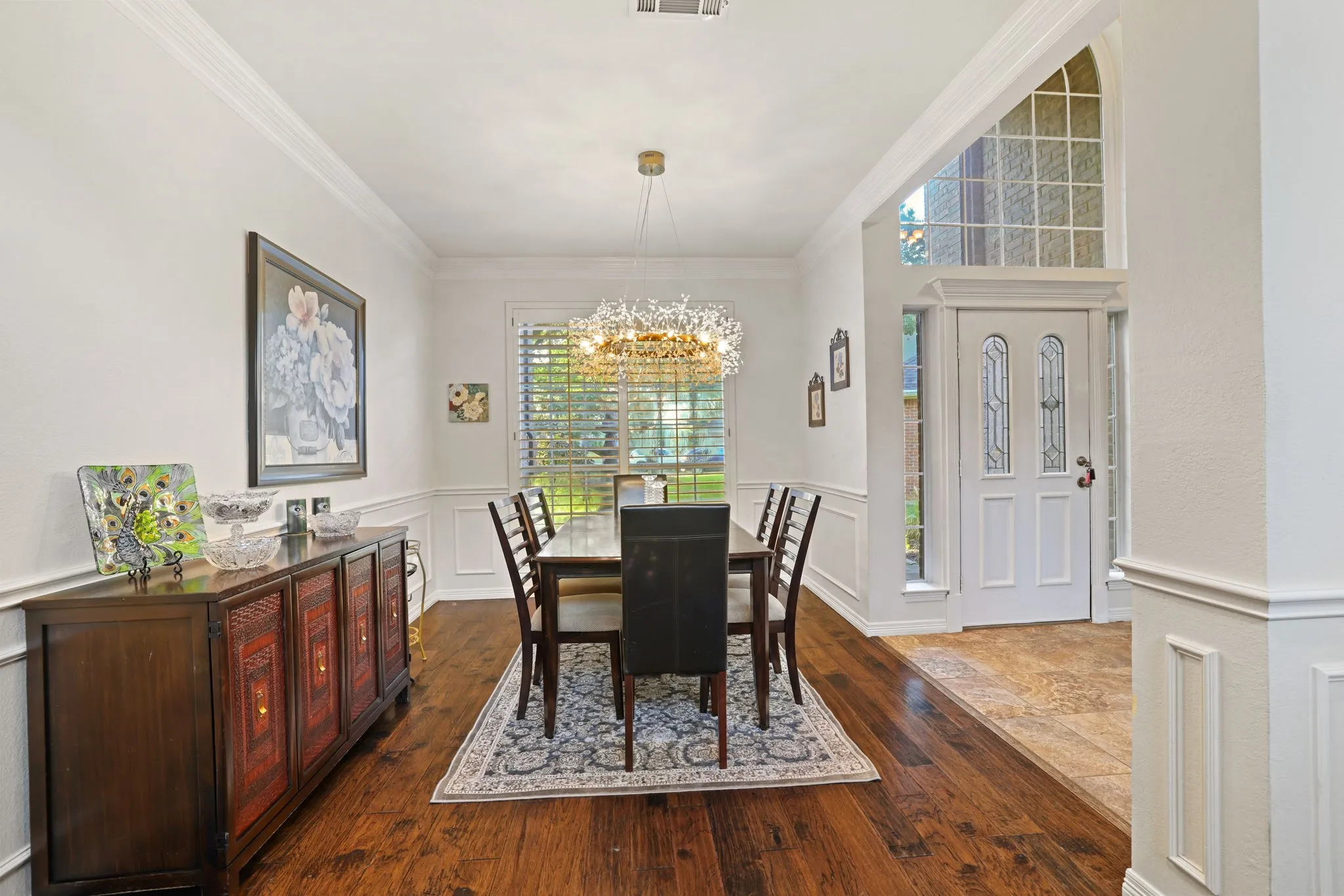 Dining area with wood-finish flooring, wainscoting, and a statement chandelier