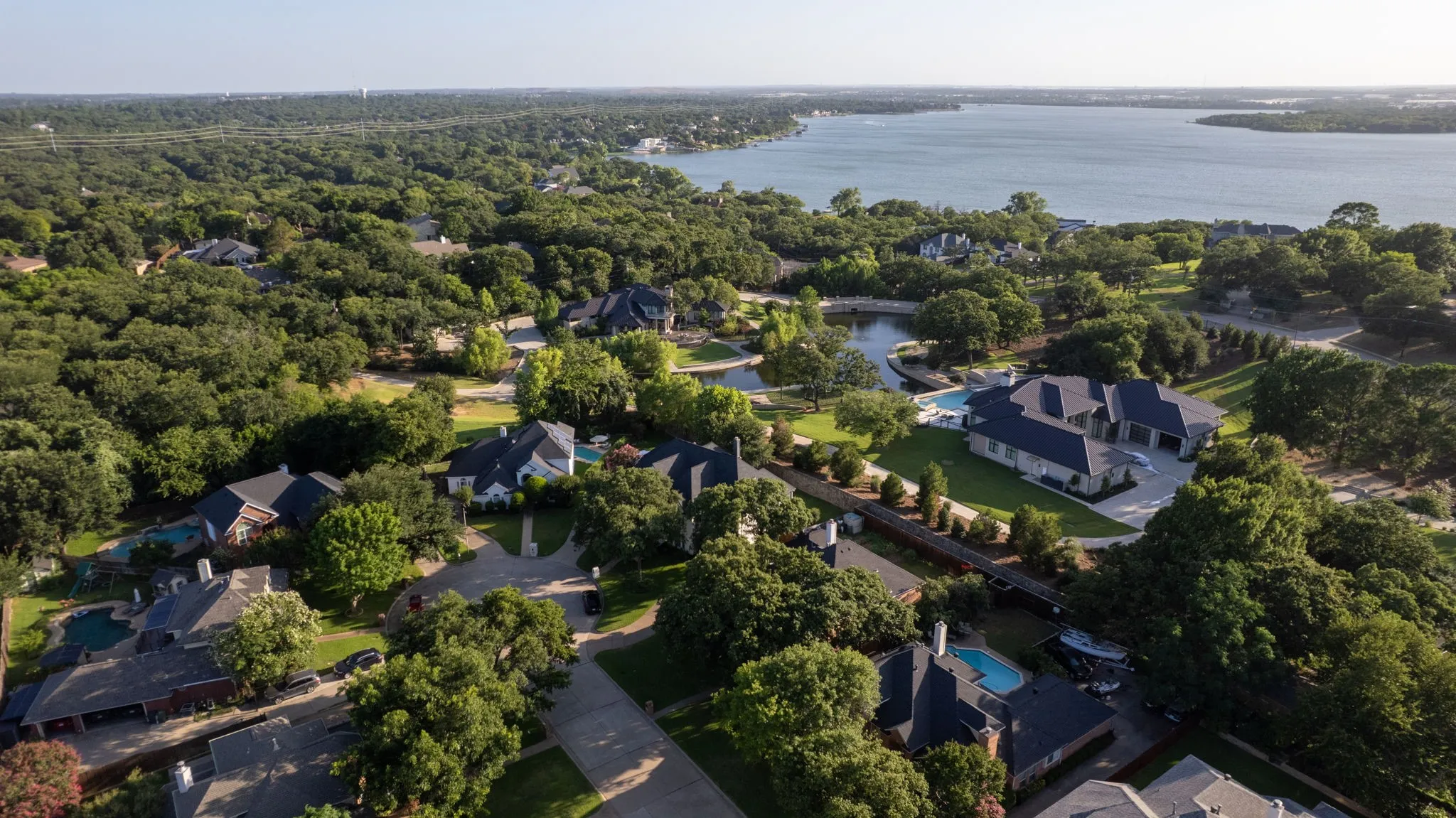 Expansive residential area featuring numerous mature trees and a substantial body of water in the background