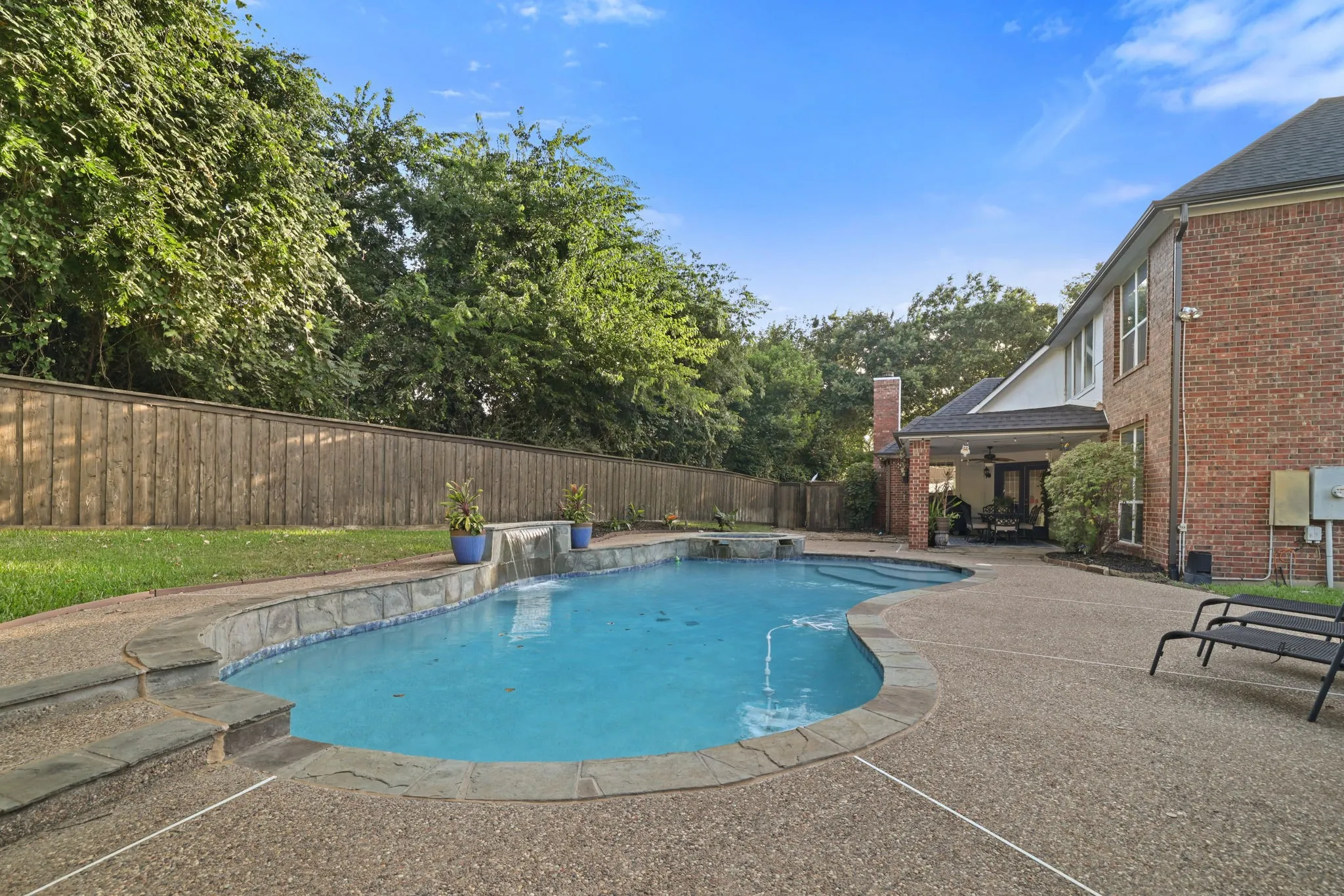 Resort-style backyard featuring a freeform swimming pool with waterfall, integrated spa, and flagstone coping
