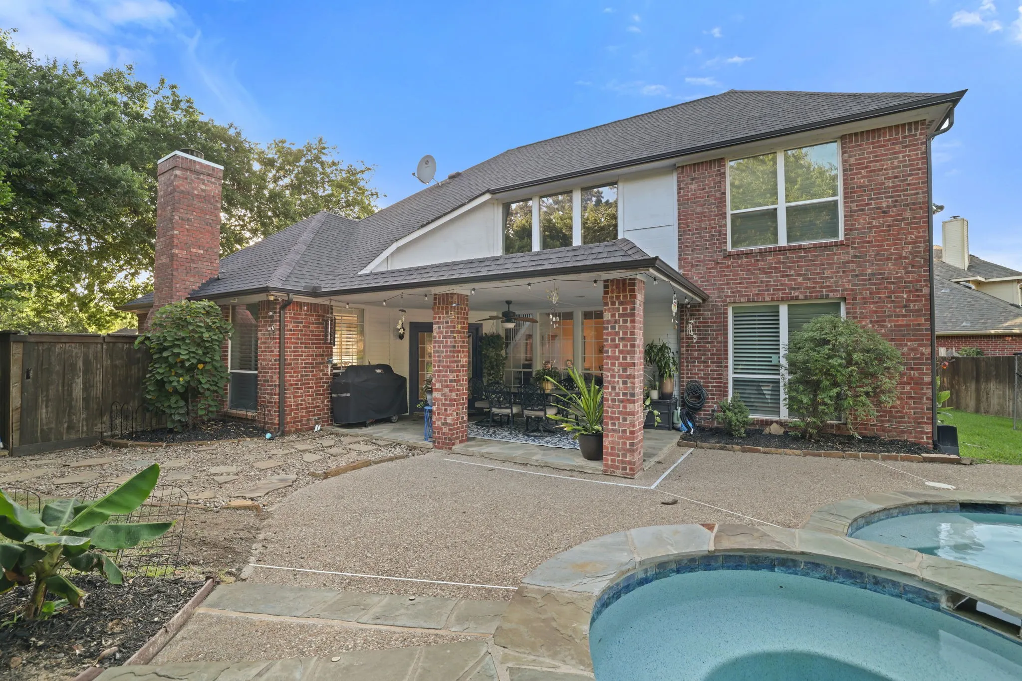 Rear exterior featuring brick facade, covered patio, integrated spa, and expansive windows