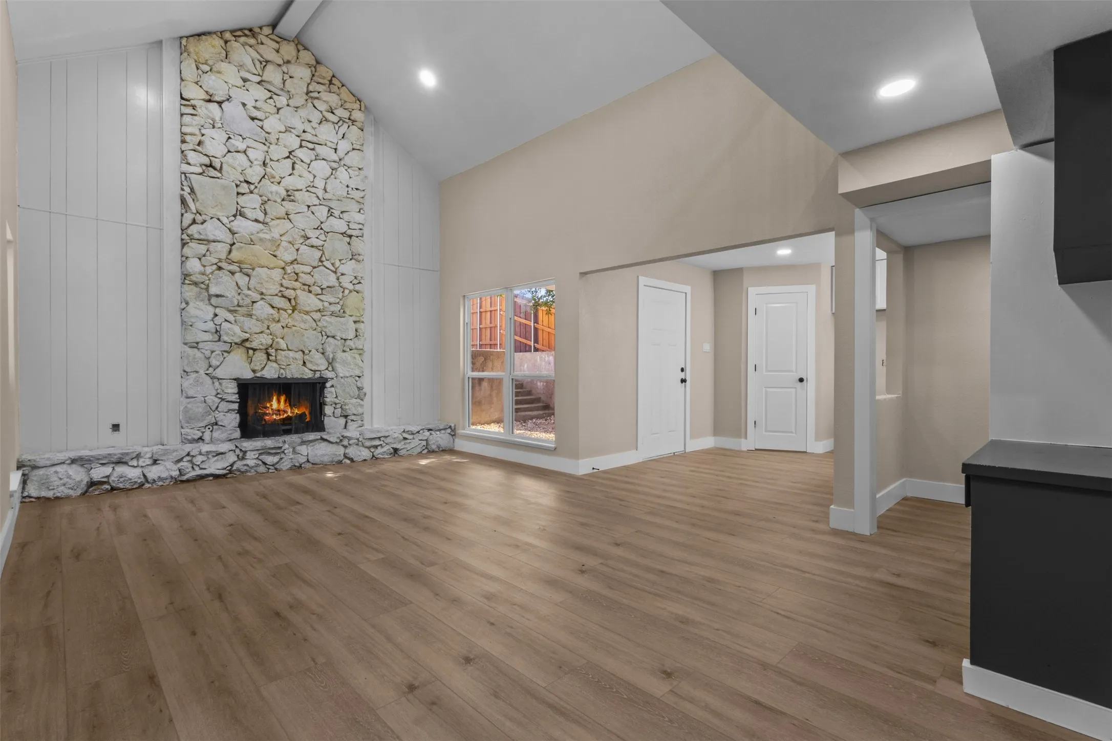 Vaulted ceiling living area featuring a full-height stone fireplace with hearth, wood-finish flooring, and recessed lighting