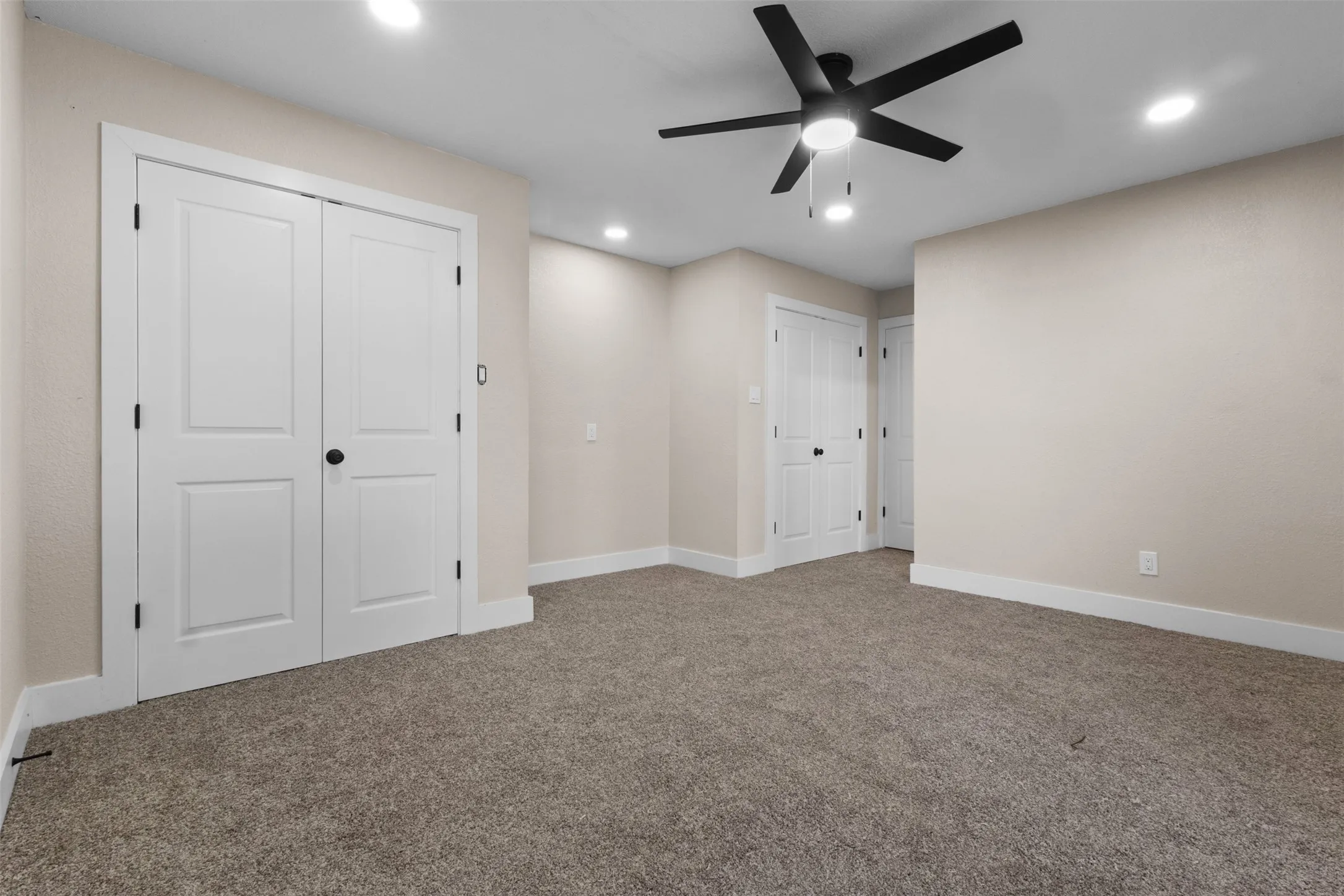 Spacious room featuring neutral carpeting, a modern black ceiling fan, recessed lighting, and white bi-fold closet doors with black hardware