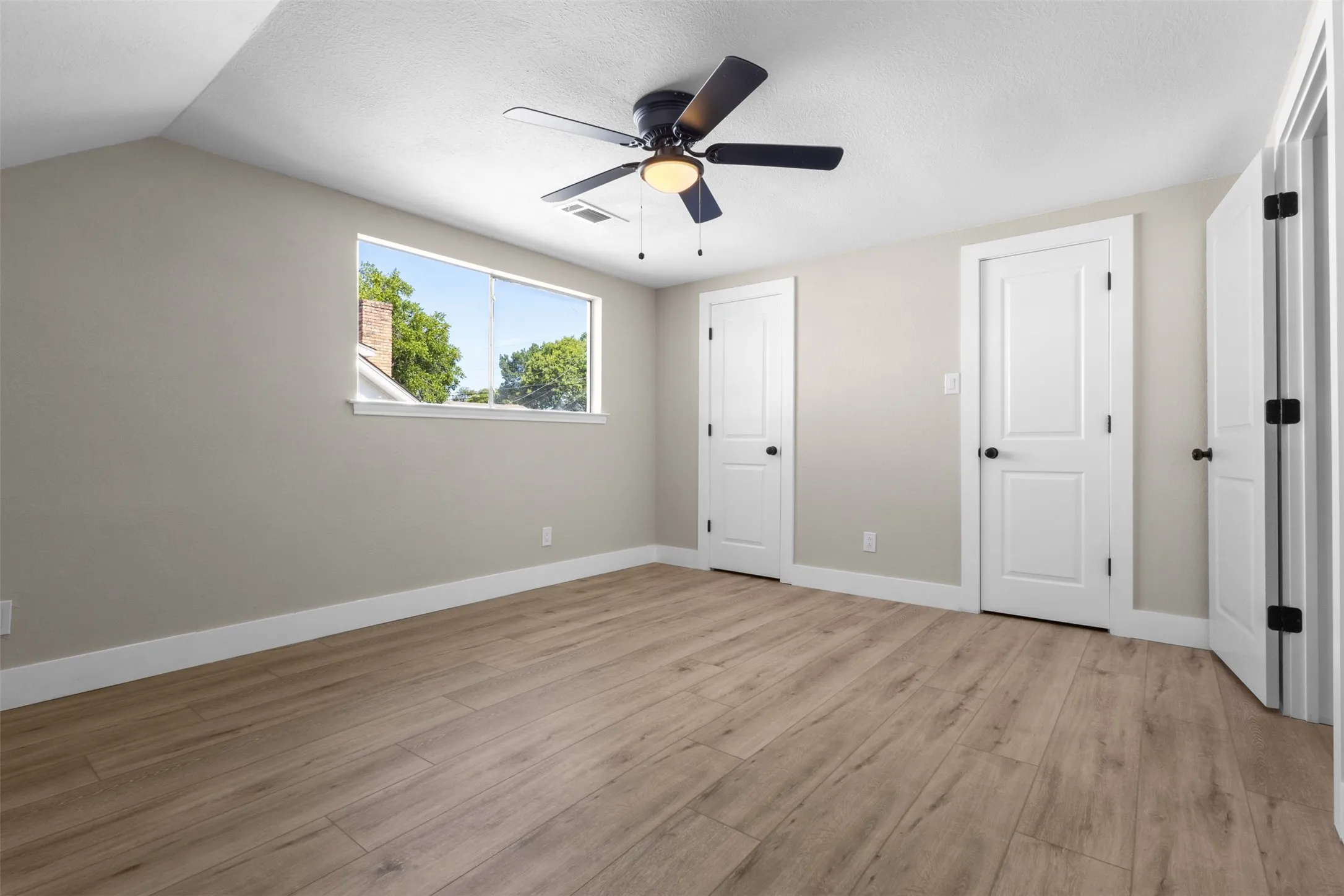 Spacious room featuring light wood-finish flooring, neutral wall tones, and multiple white paneled doors