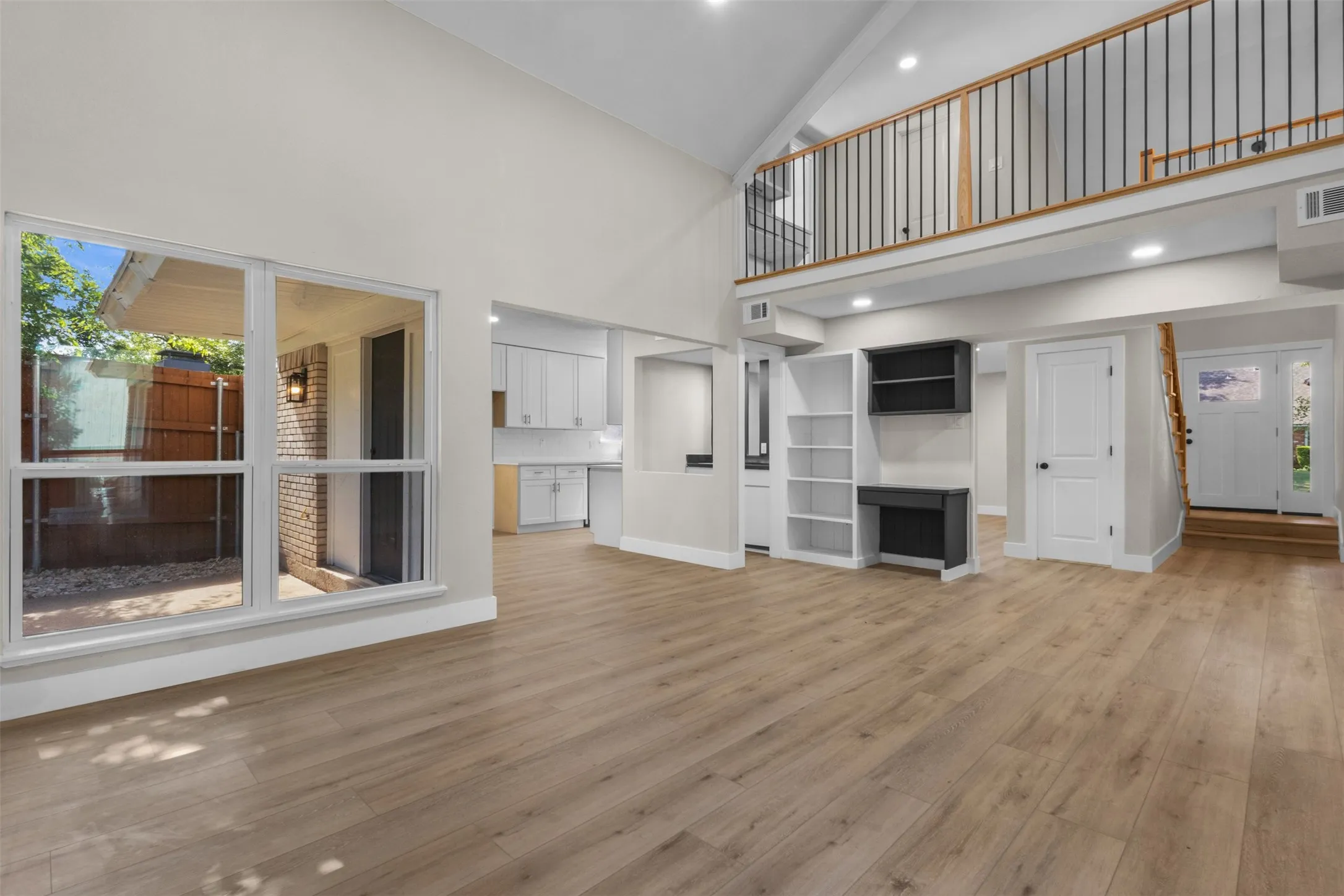 Spacious interior featuring wood-finish flooring, vaulted ceilings, and a large window overlooking a private patio area