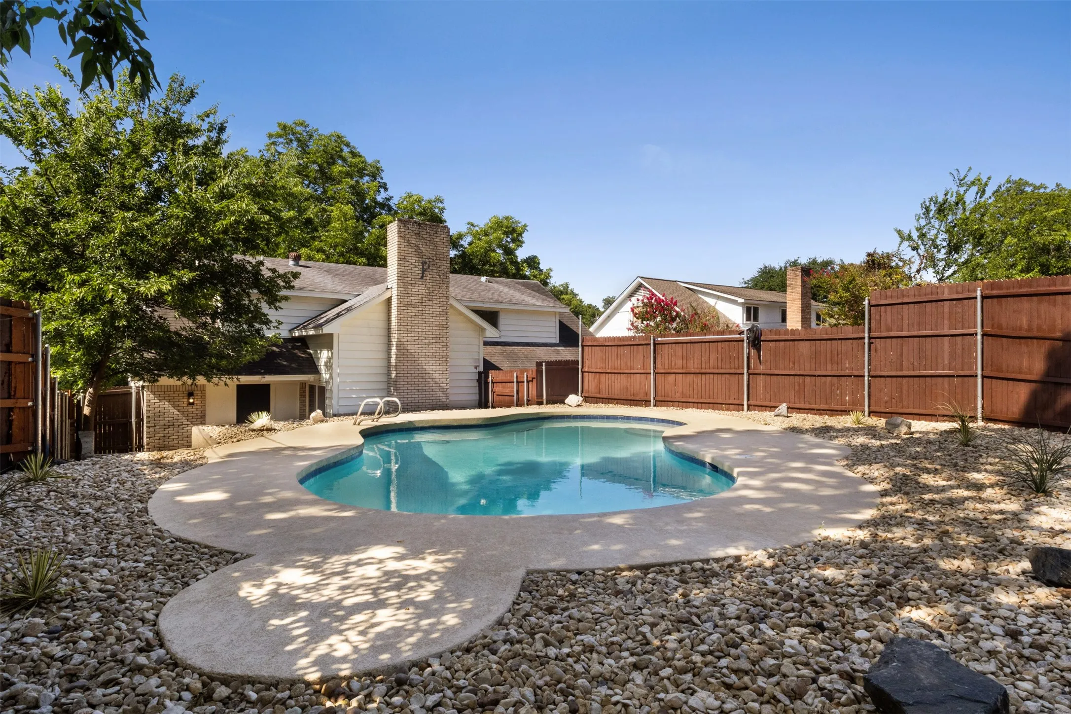 Inviting backyard features a freeform swimming pool with a concrete surround, surrounded by decorative rock landscaping