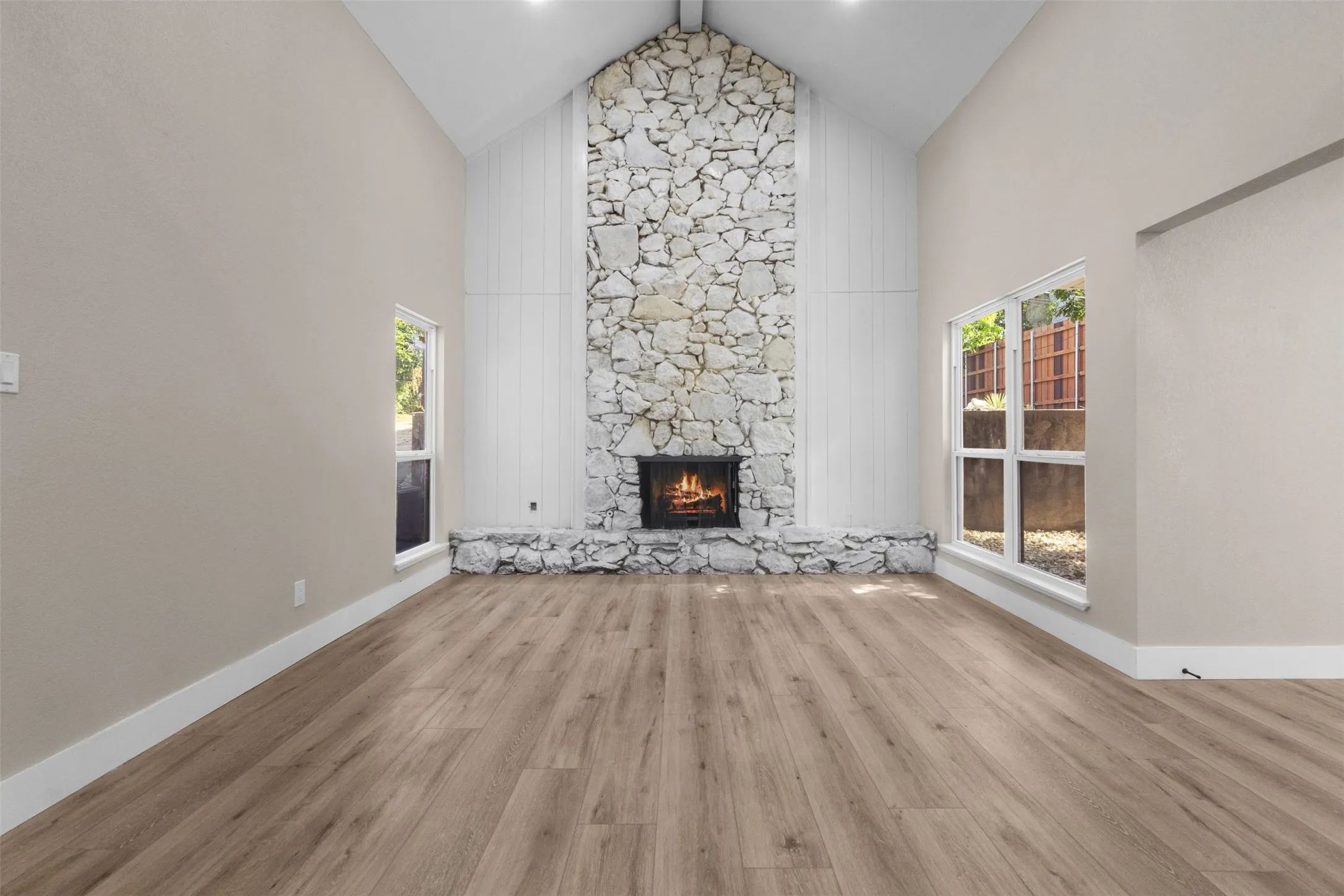 Living area with vaulted ceilings, a floor-to-ceiling stone fireplace, and wood-finish flooring