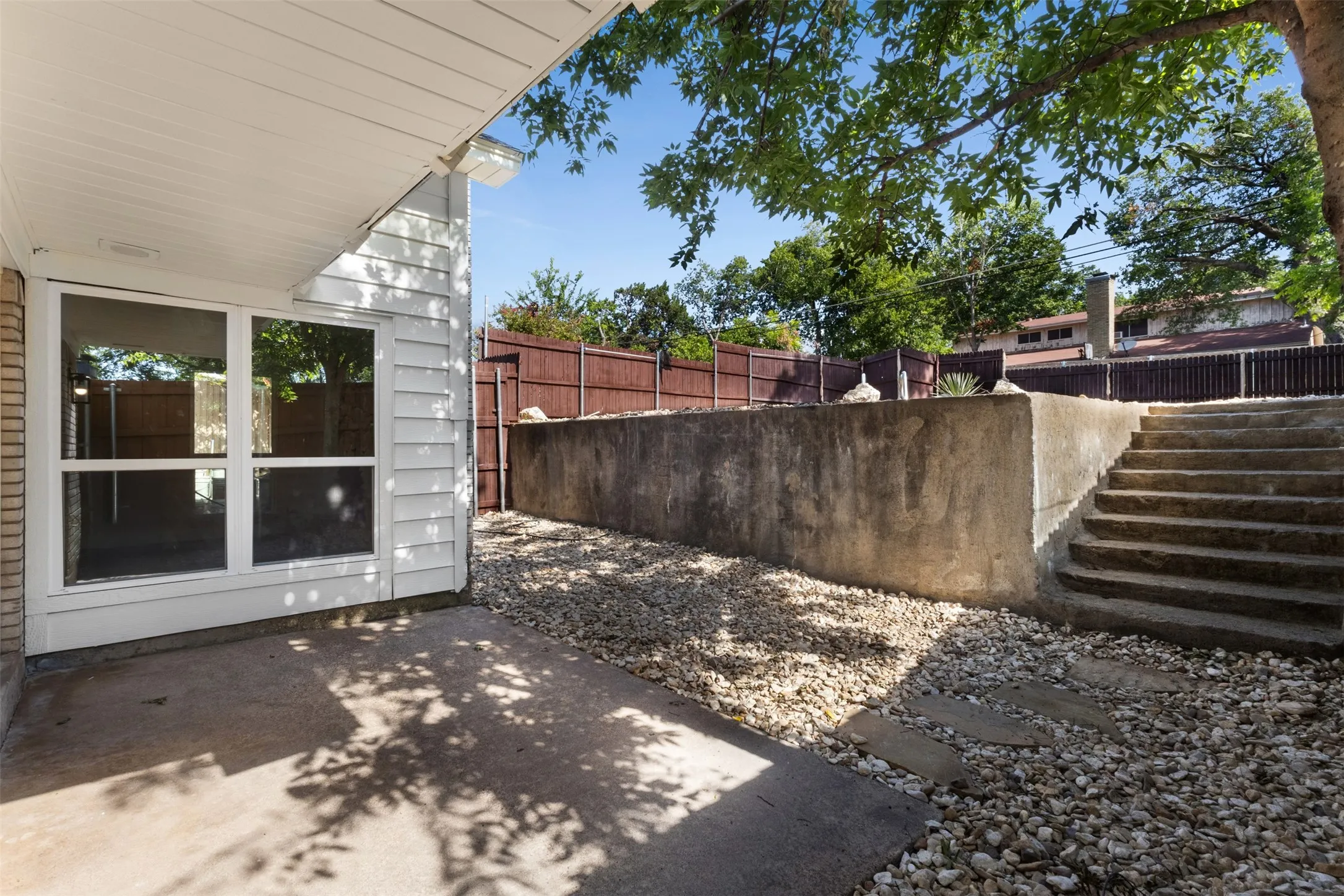Exterior patio with a concrete surface, featuring a windowed wall, white siding, and brick accents