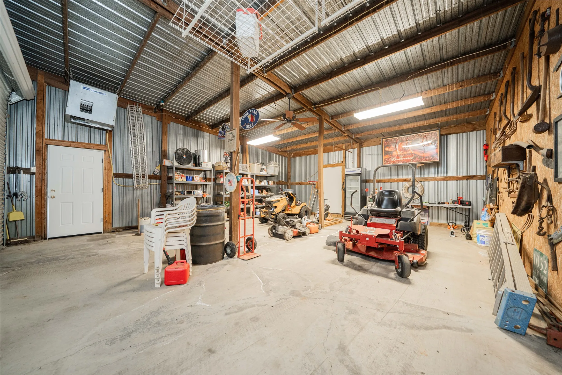 Spacious outbuilding featuring a concrete floor, exposed wood beam framing, corrugated metal walls and ceiling, and multiple fluorescent light fixtures