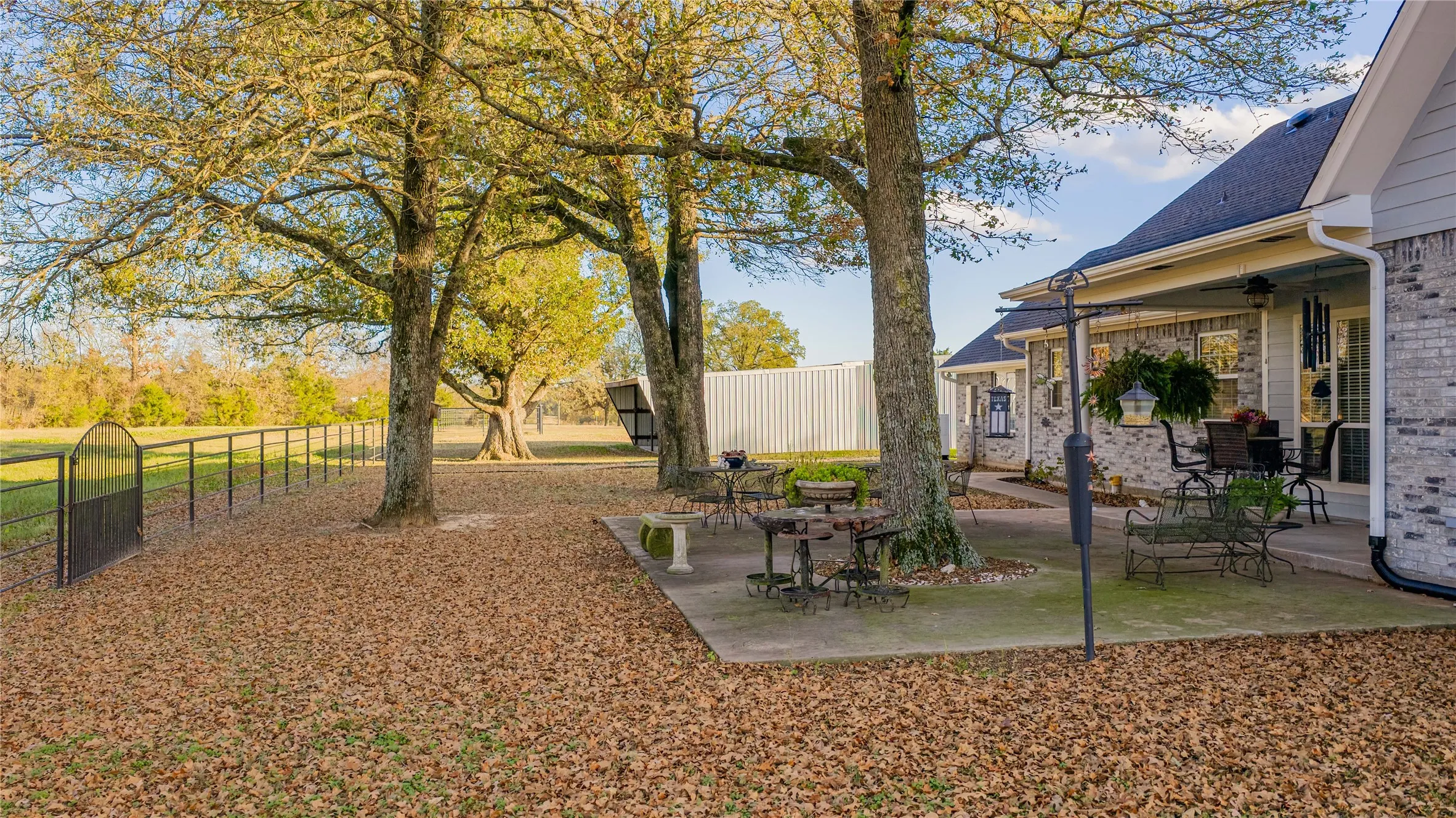 Rear exterior featuring a covered patio, extensive concrete hardscaping, and mature trees