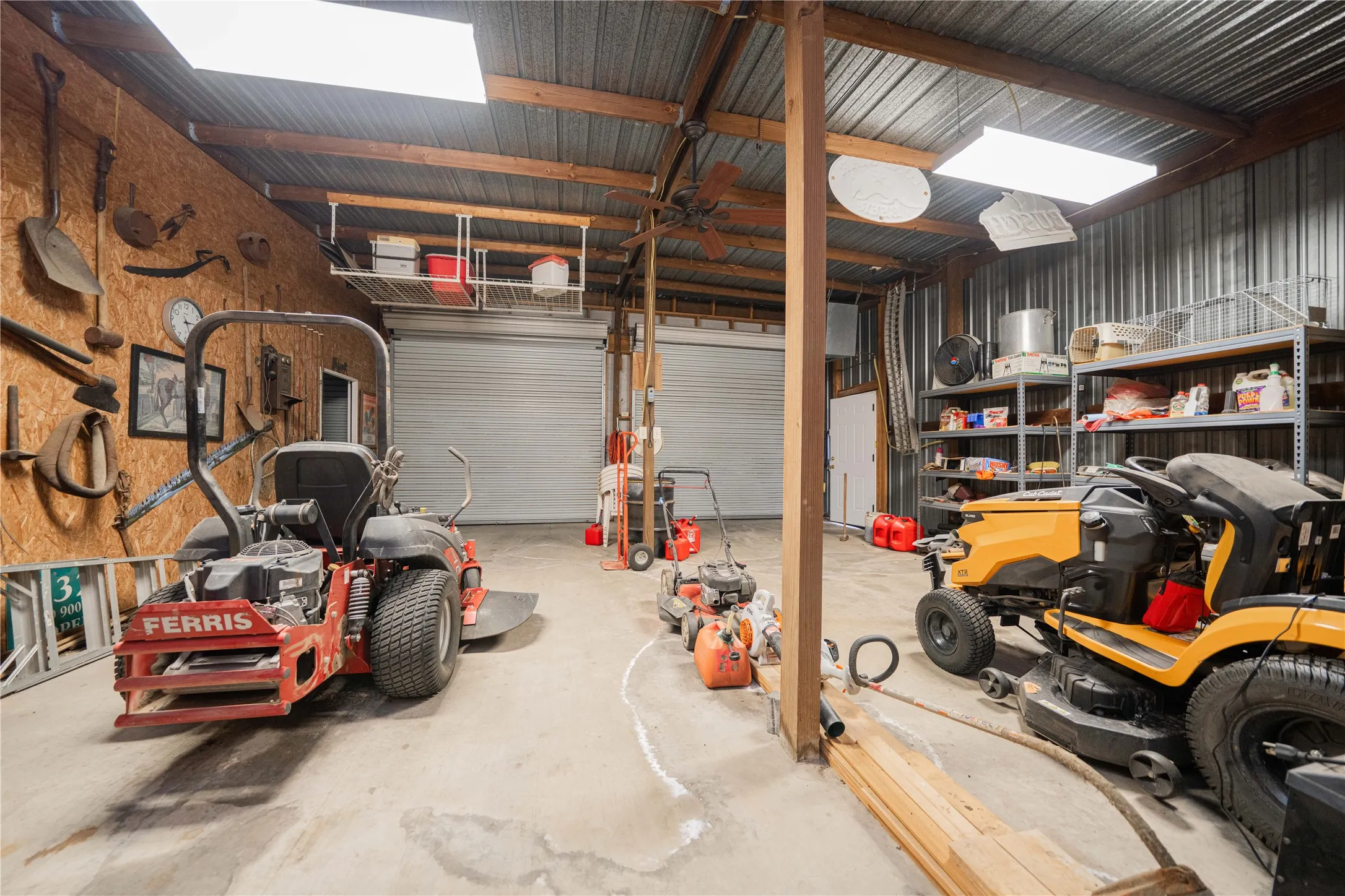 Spacious utility building featuring two roll-up doors, exposed wood beam construction, corrugated metal walls, and a concrete floor