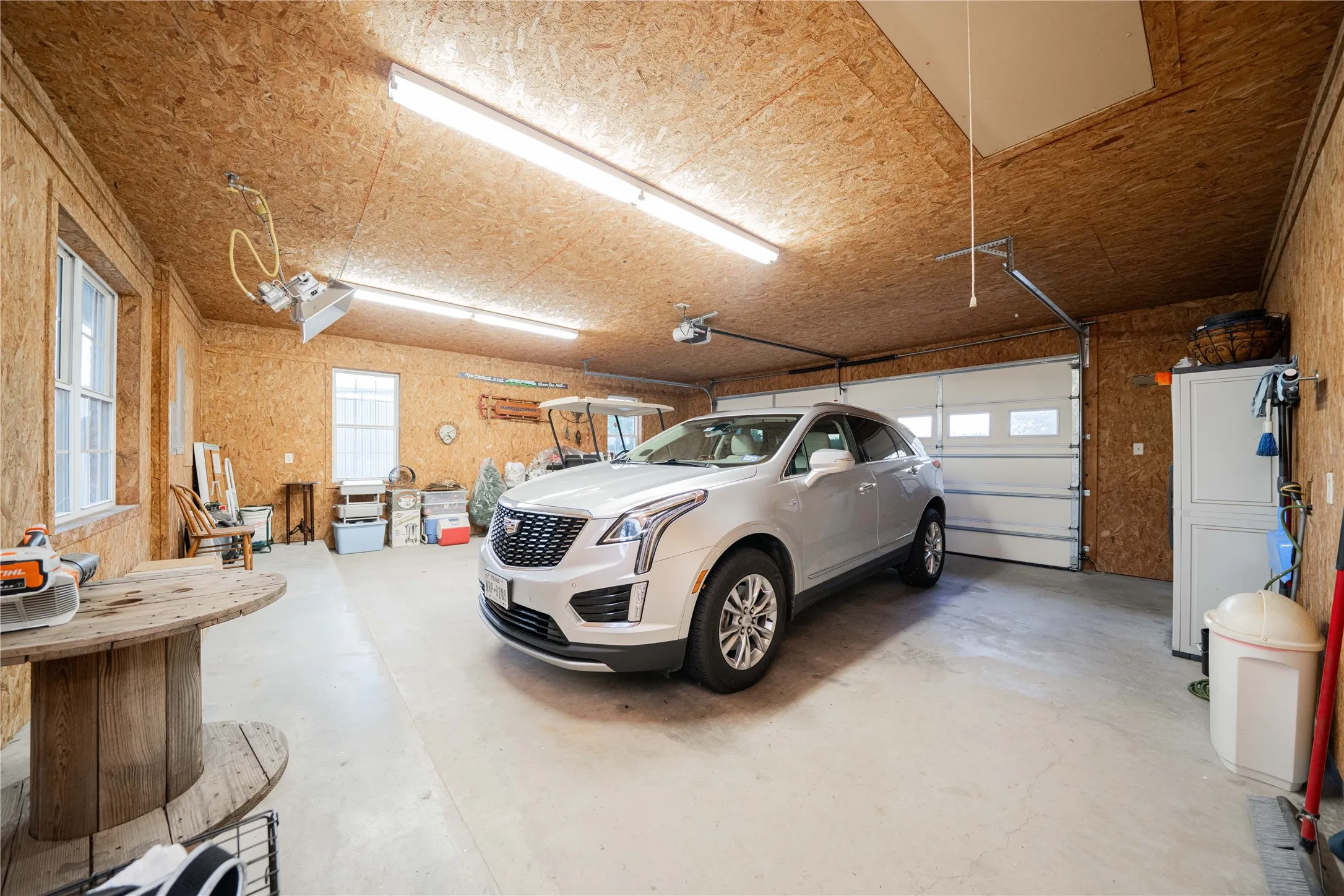 Spacious garage featuring a light-colored concrete floor, light wood-finish walls and ceiling, two multi-pane windows, and a segmented garage door with upper window panels