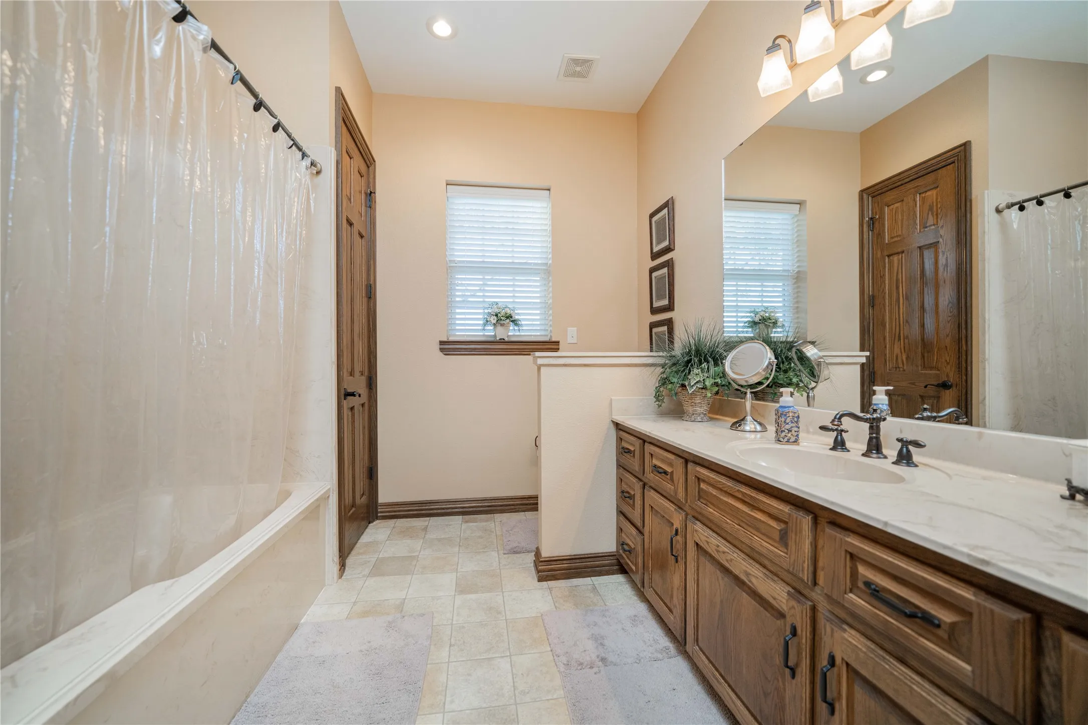 Bathroom featuring a long wood-finish vanity with dual sinks and a light-colored countertop