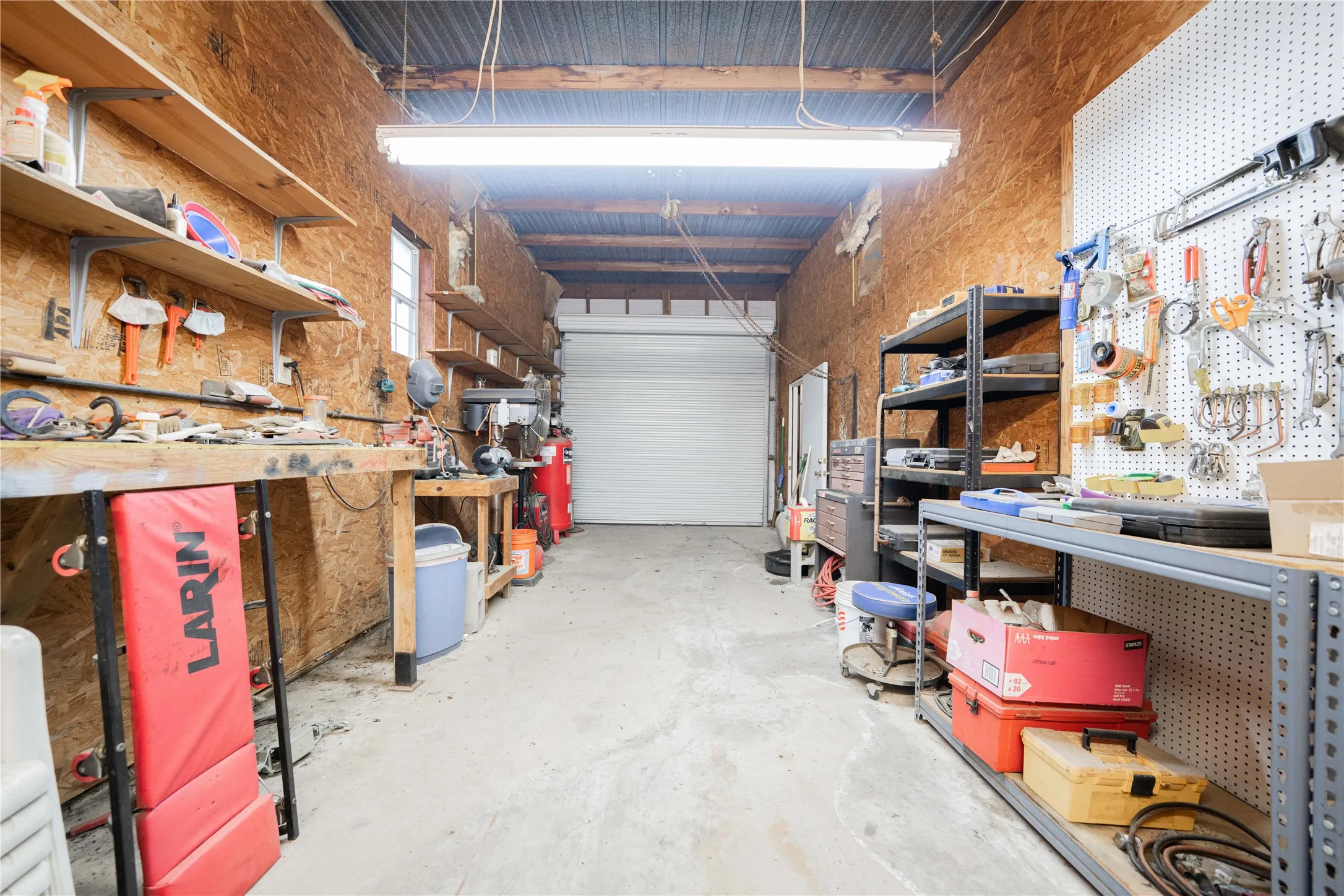 Open workshop space with concrete flooring, exposed wood-finish walls, and an overhead roll-up door