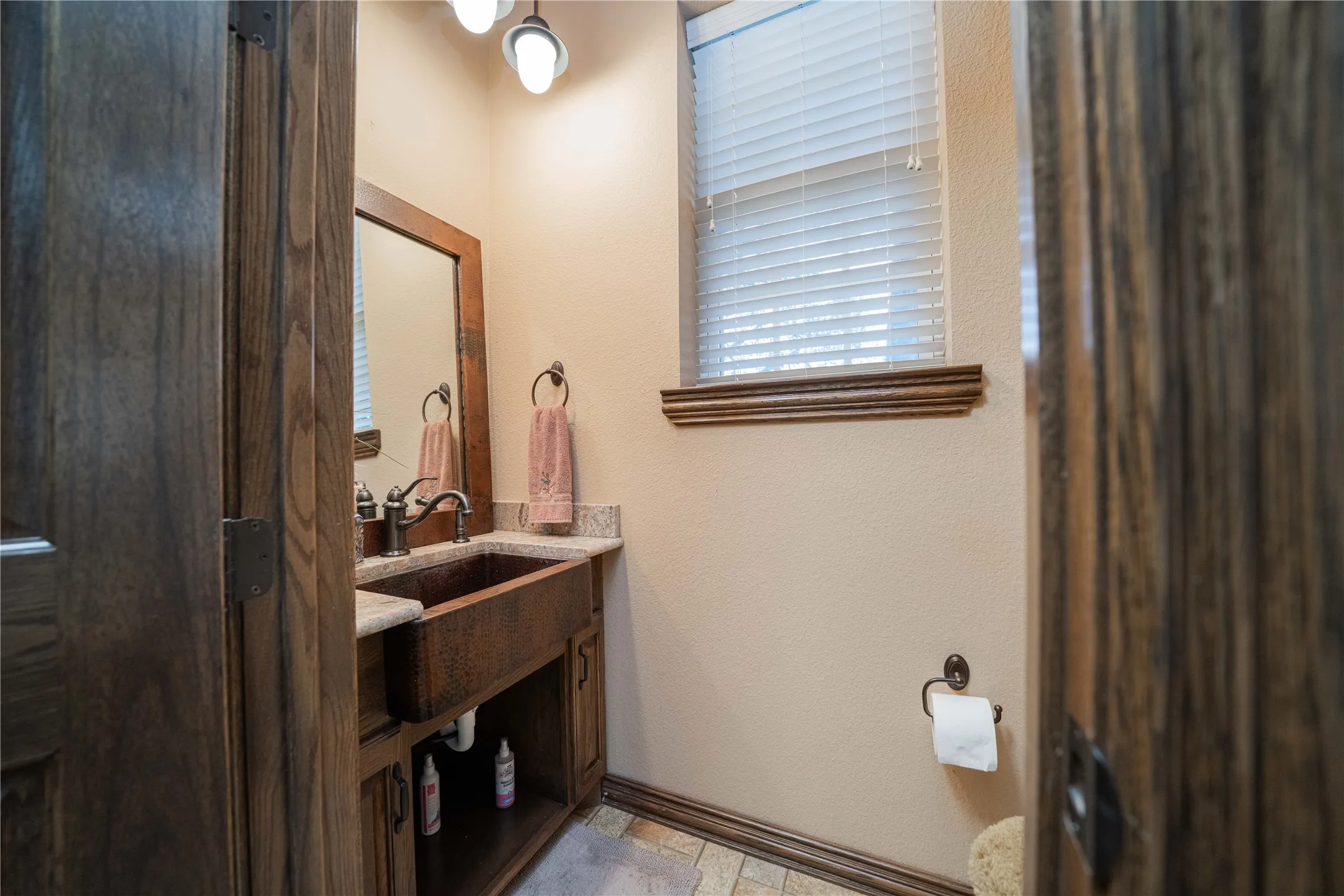 Bathroom vanity featuring a vessel sink with a bronze finish, light-toned countertop, and dark wood-finish cabinetry