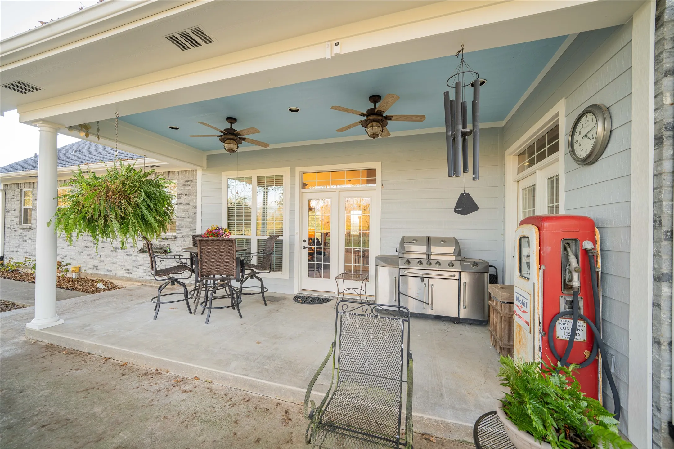 Covered concrete patio featuring two ceiling fans with light kits, a light blue ceiling, white columns, and double French doors with transom windows