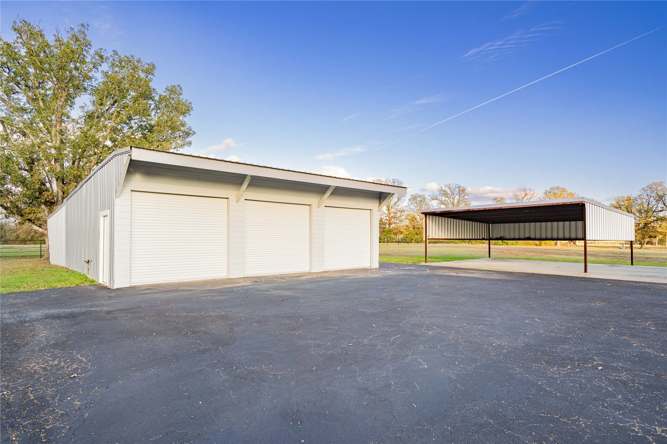 Three-bay garage with roll-up doors, an additional covered carport, and extensive paved parking area