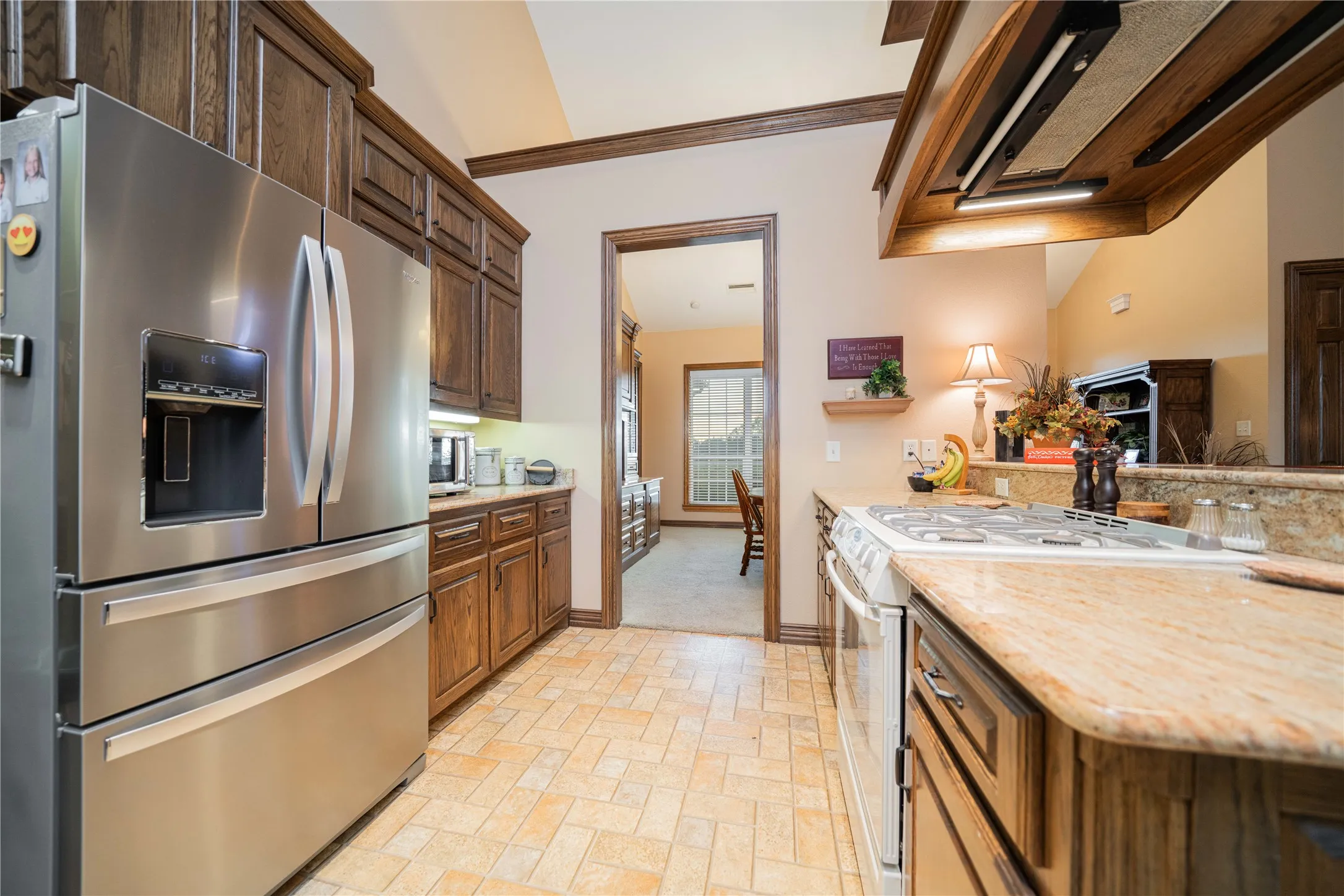 Kitchen featuring wood cabinetry, stainless steel refrigerator, white gas range, and stone-finish countertops