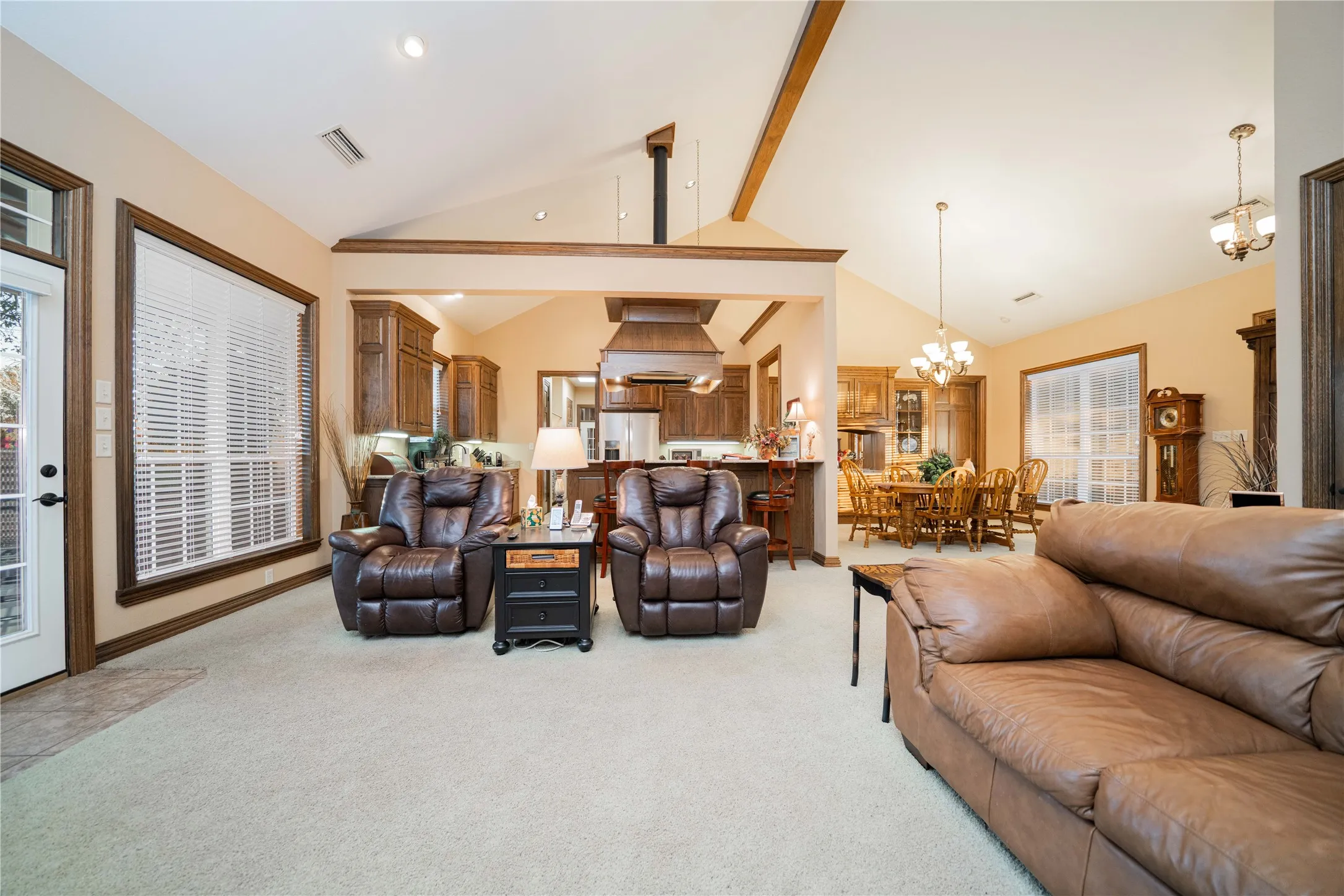 Carpeted living area featuring vaulted ceilings with exposed beams, large windows, and a glass-paneled exterior door