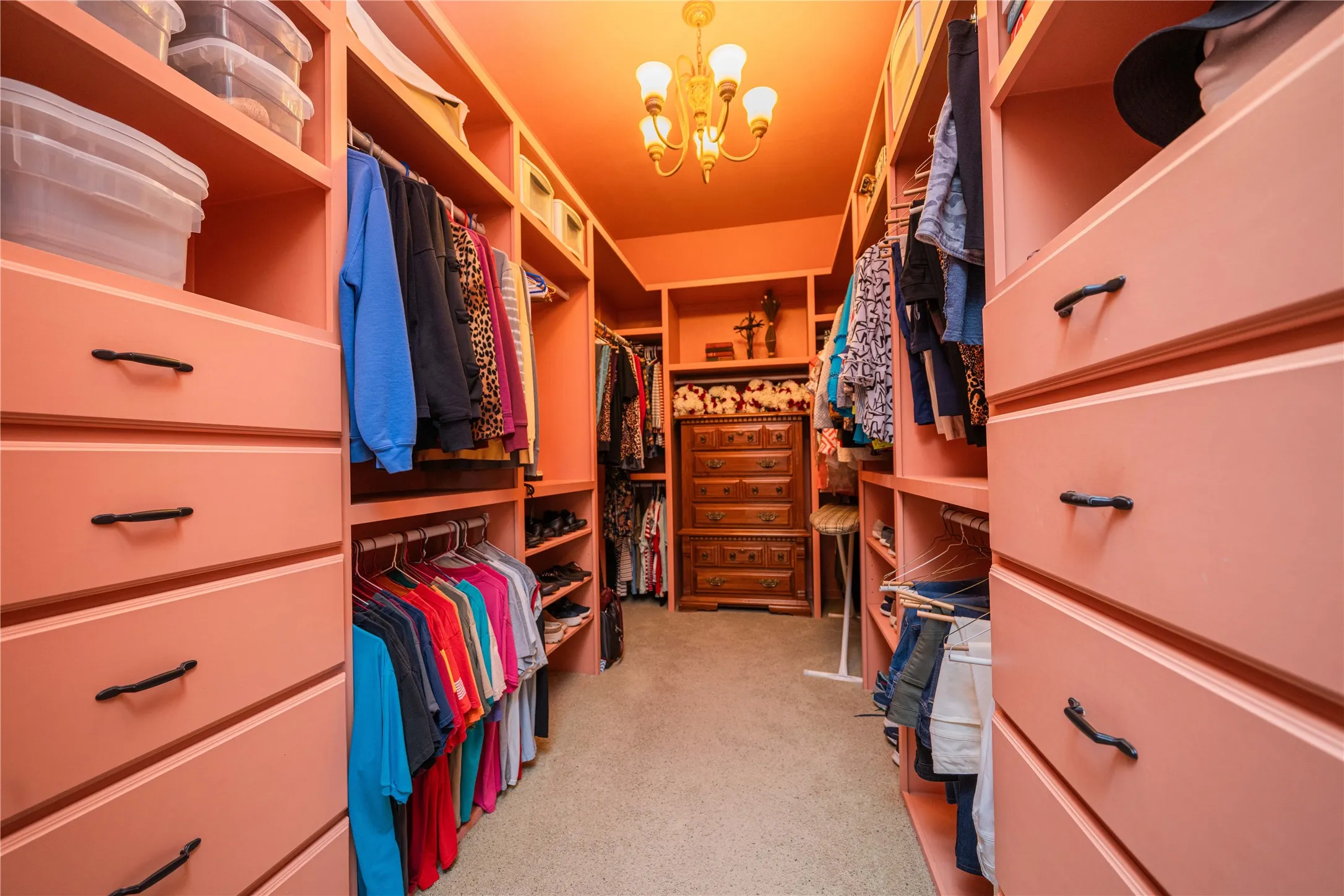 Walk-through closet featuring custom built-in cabinetry, varied shelving, garment hanging rods, integrated drawer storage, and a central chandelier