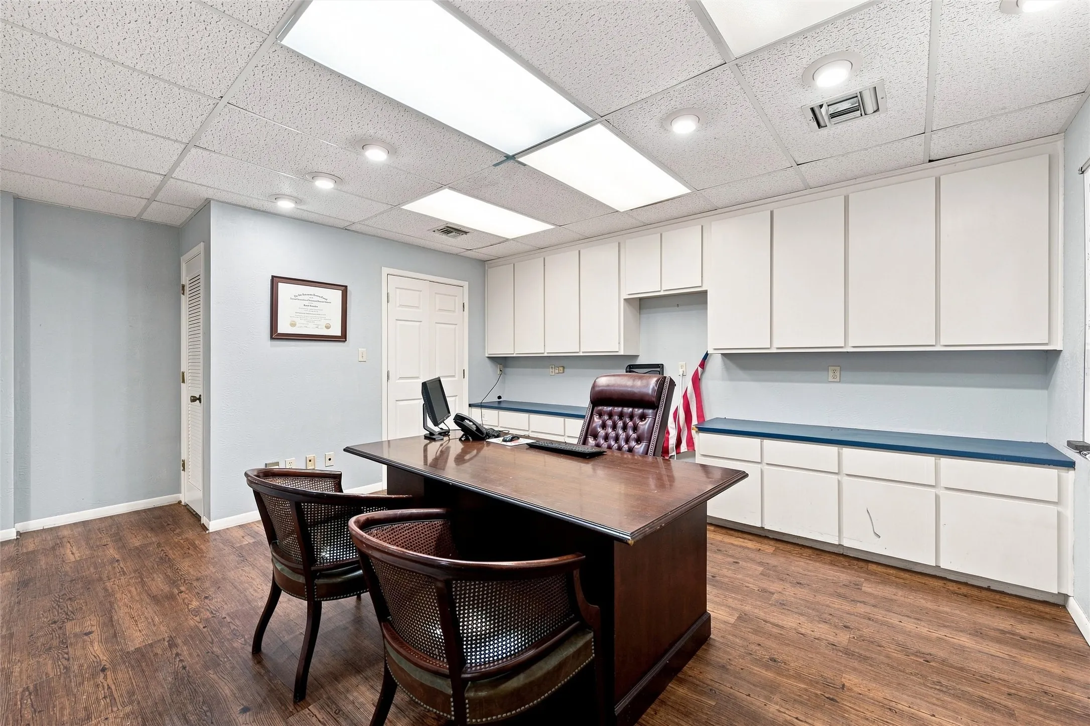 Office space featuring wood-finish flooring, extensive built-in white cabinetry, a built-in blue countertop, and recessed lighting