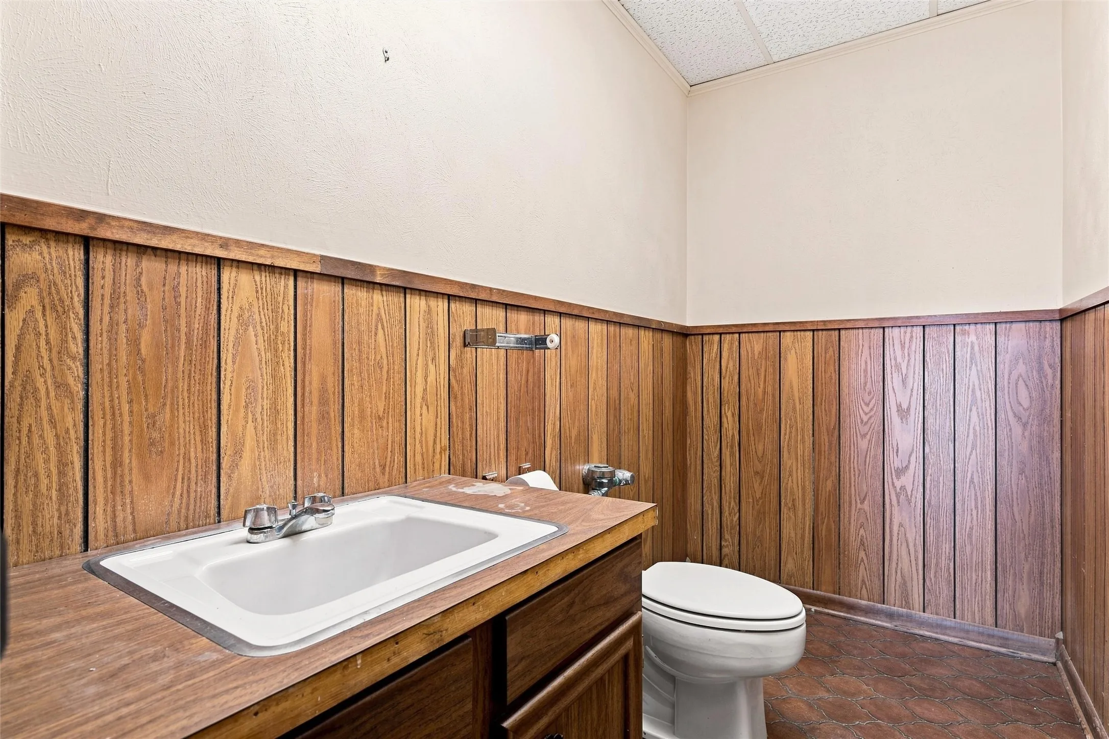 Bathroom featuring wood-finish paneling, an integrated sink vanity with a laminate countertop, and a white toilet