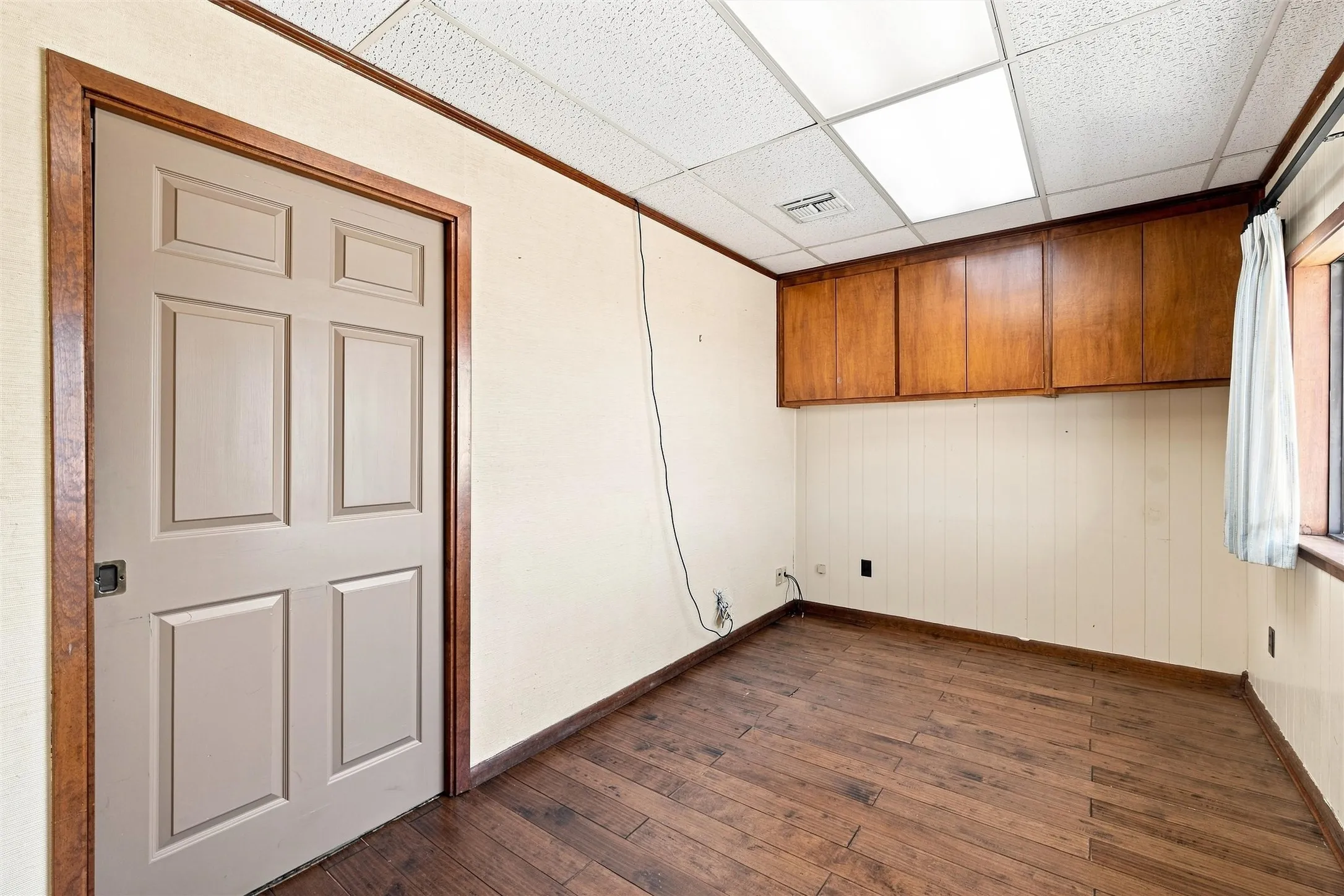 Room featuring wood-finish flooring, built-in upper cabinetry, paneled walls, and a drop ceiling with recessed lighting