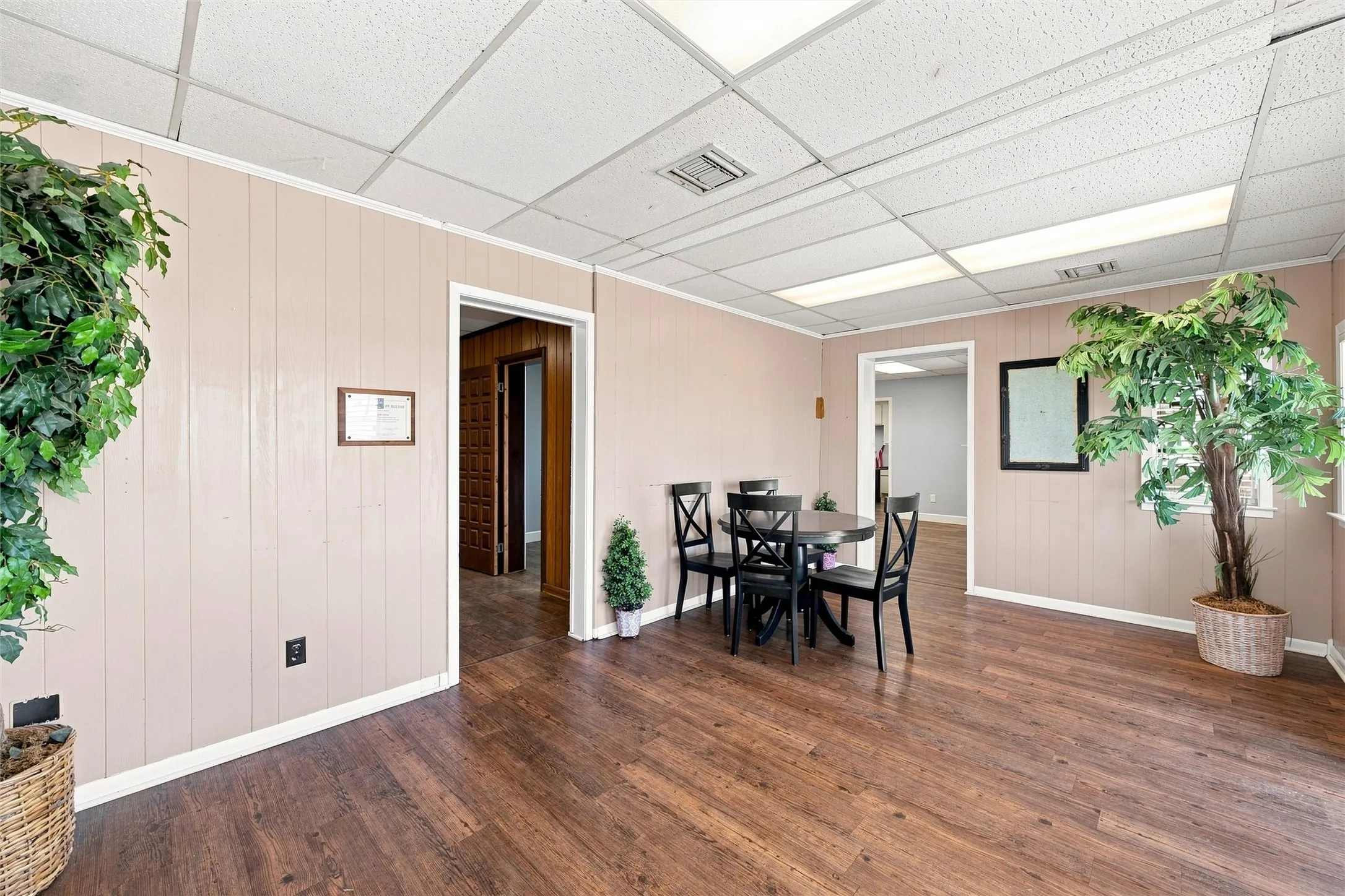 Spacious room featuring wood-finish flooring, light-colored vertical wall paneling, and a grid ceiling with integrated lighting