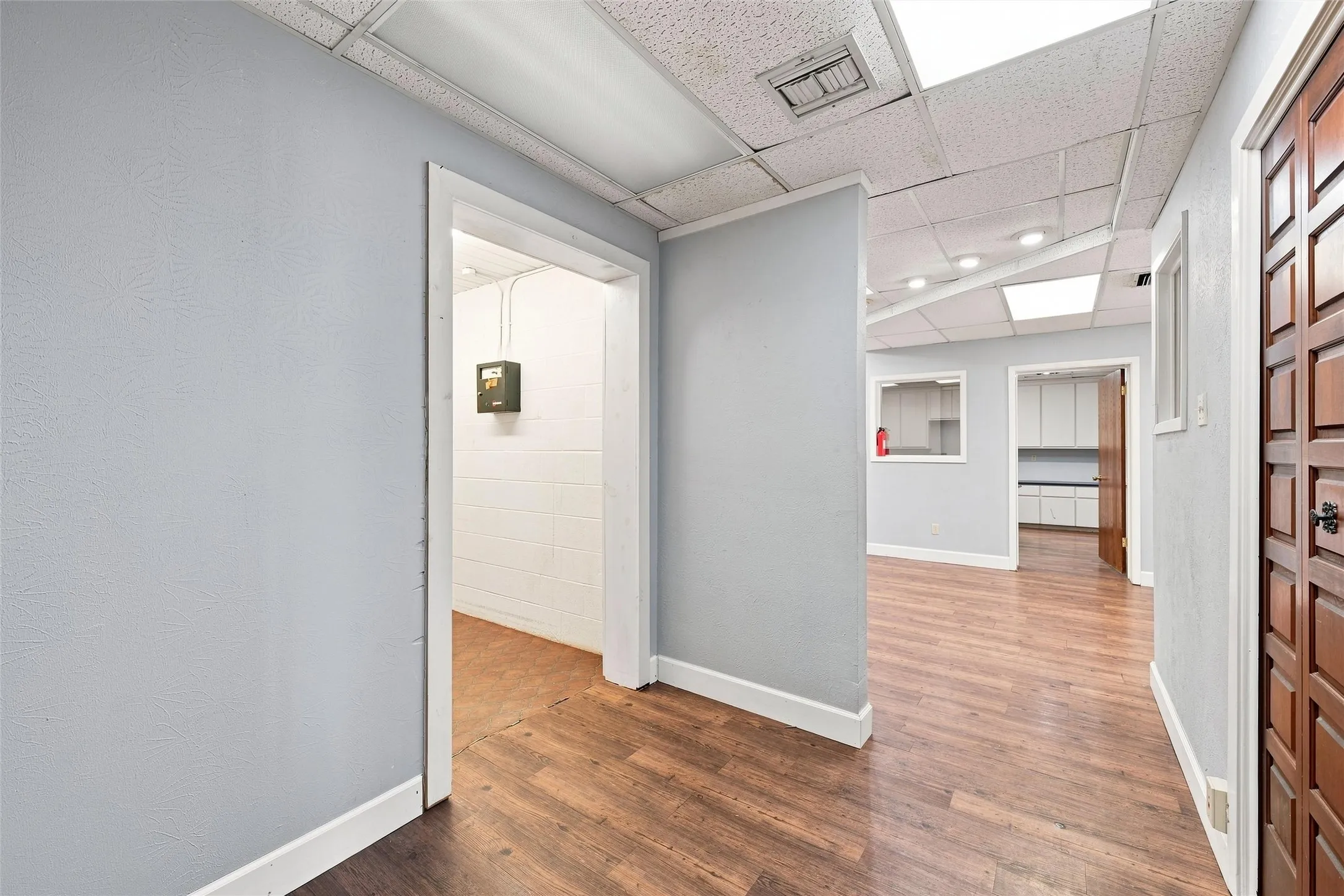 Interior space featuring wood-finish flooring, light gray walls, and a drop ceiling with recessed lighting
