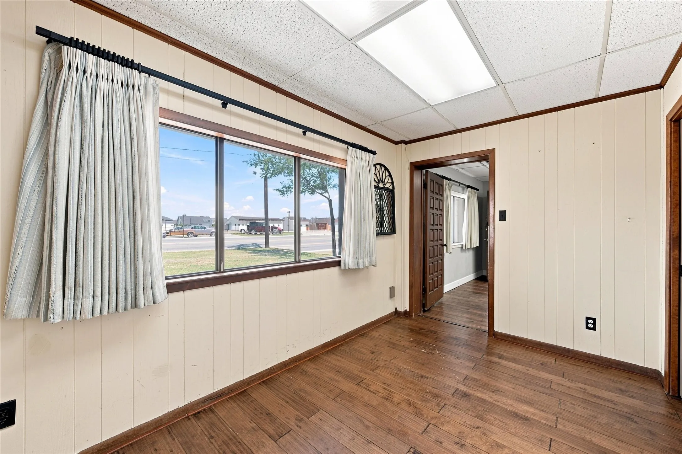Room featuring wood-finish flooring, light-toned vertical paneling, and a drop ceiling with integrated lighting