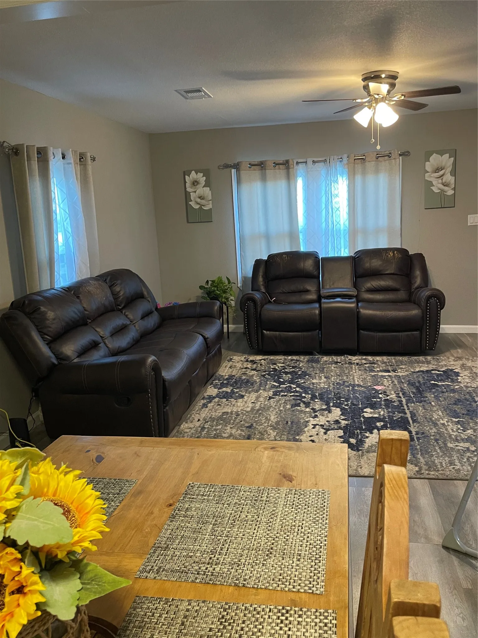 Living area featuring light gray walls, wood-finish flooring, a ceiling fan with integrated lighting, and multiple windows