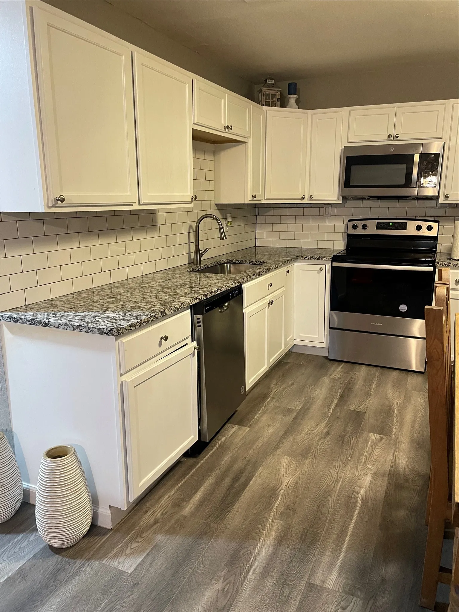 Modern kitchen featuring white cabinetry, subway tile backsplash, stainless steel appliances, speckled countertops, and wood-finish flooring
