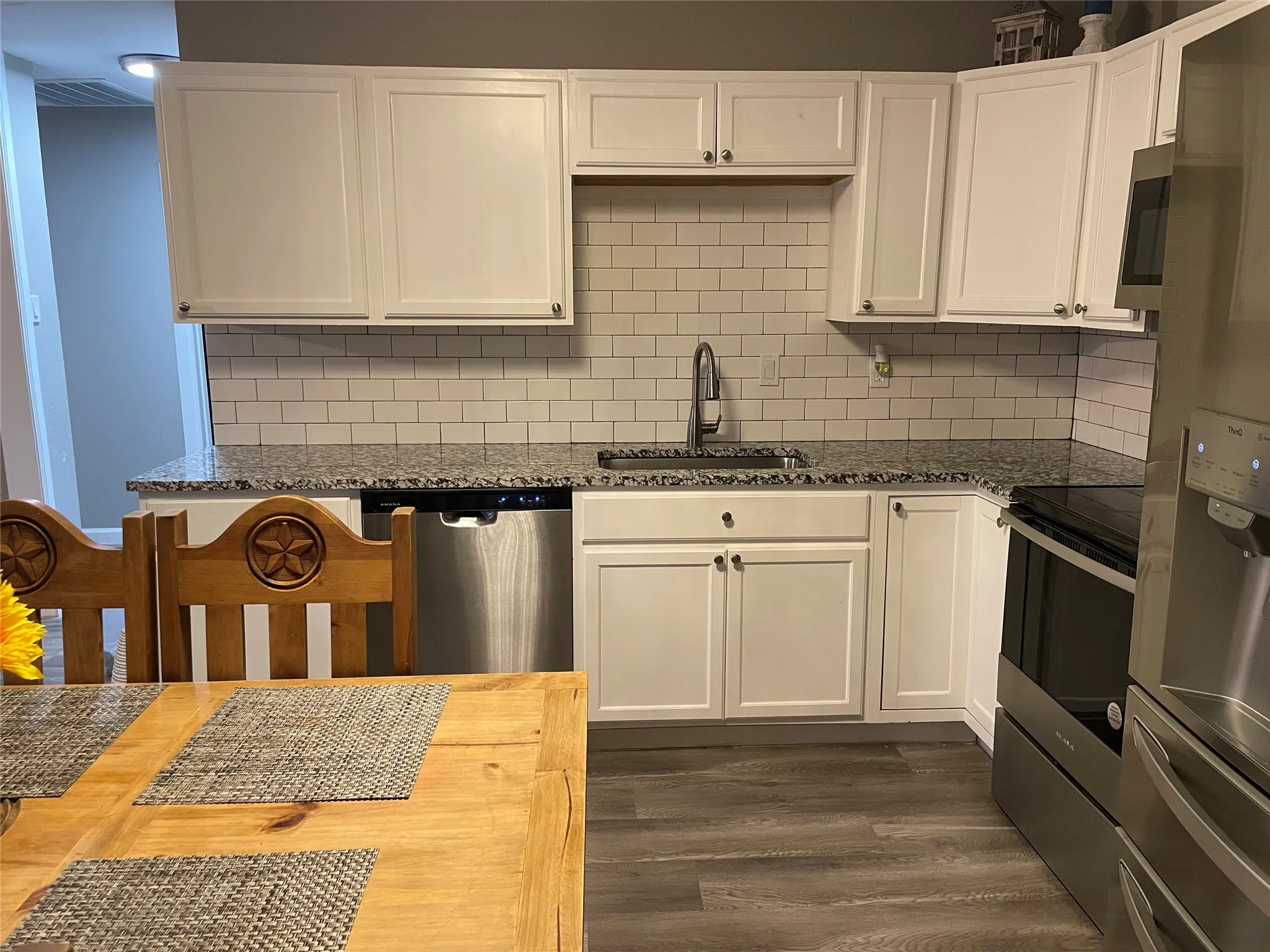 Kitchen featuring white shaker-style cabinetry, granite countertops, subway tile backsplash, stainless steel appliances, and wood-finish flooring