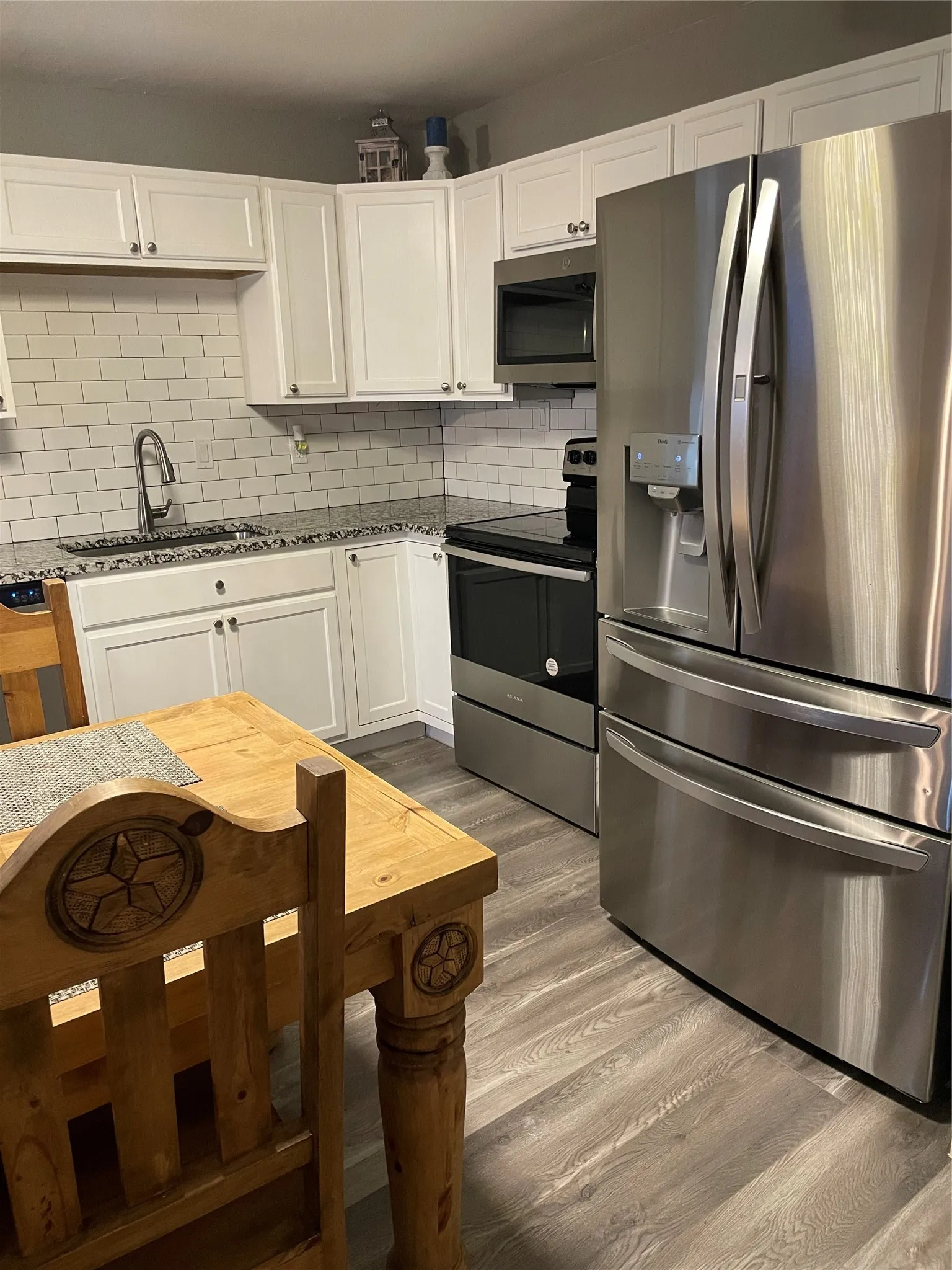 Kitchen featuring white shaker cabinetry, subway tile backsplash, stainless steel appliances, granite-look countertops, and wood-finish flooring