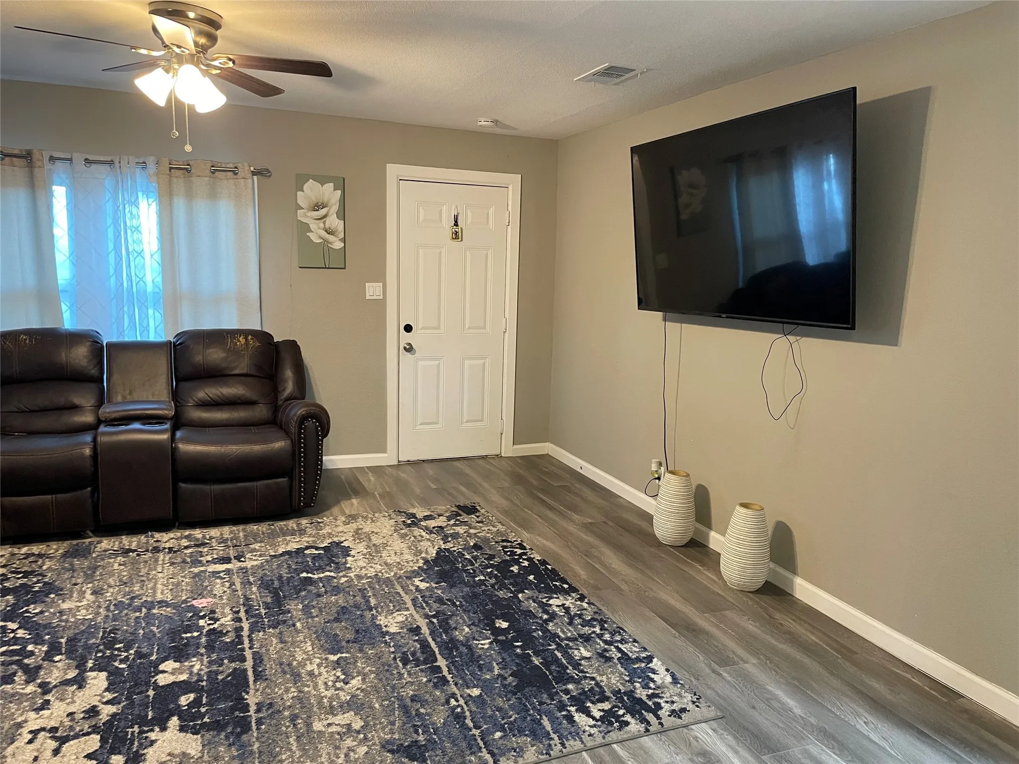 Living area featuring wood-finish flooring, a ceiling fan with integrated lighting, and a white paneled door