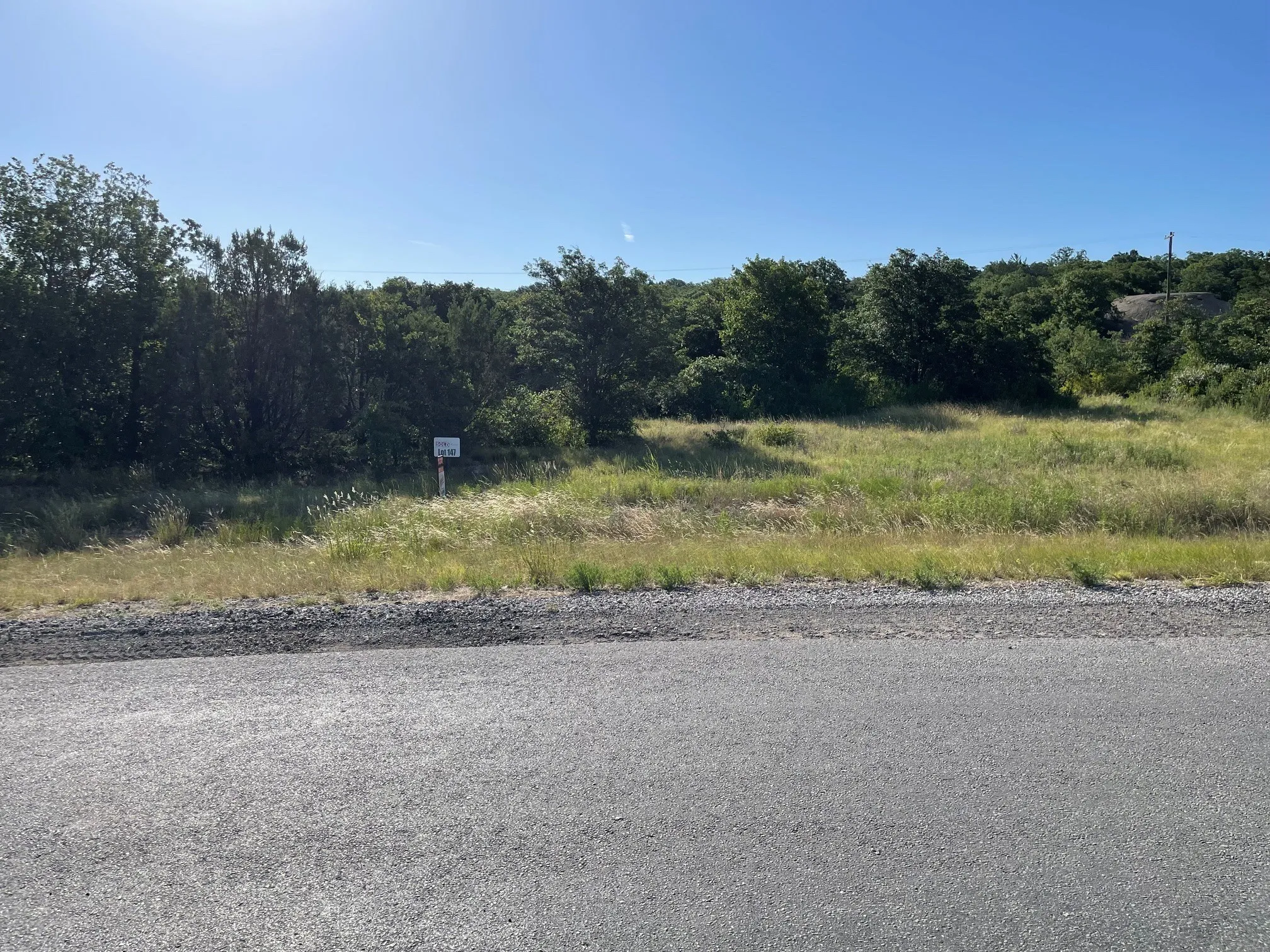 Expansive undeveloped lot featuring a mix of mature trees and open grassy areas, with direct frontage to a paved road